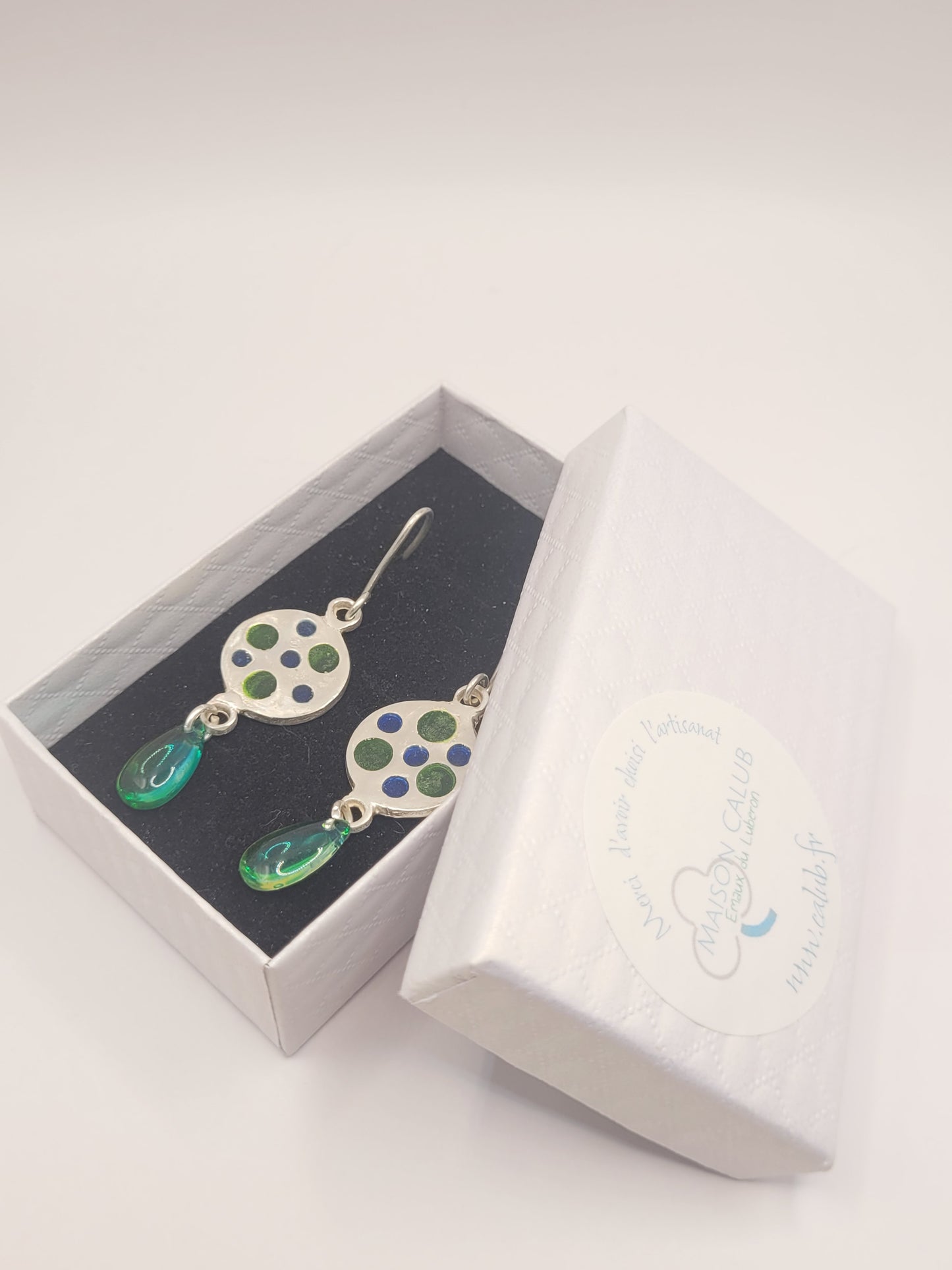 dans une boite cadeau les boucles d'oreilles uniques en émail sur qrgent fin plique-à-jour émaux translucides bleus et vert. Le pendant est prolongé par une perle de verre verte. Bijou artisanal made in France dans les ateliers du Luberon Maison Calub en Provence