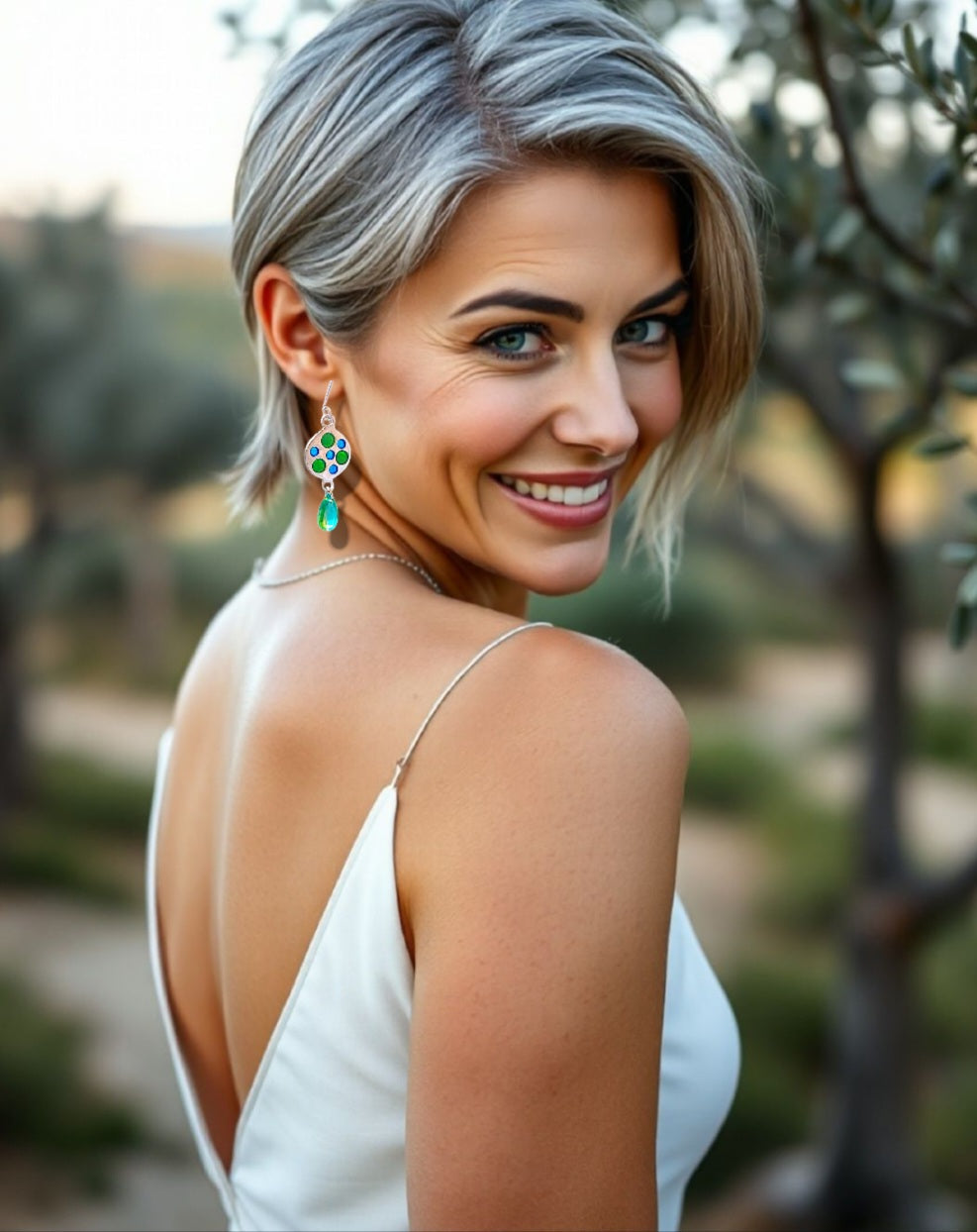 femme portant les boucles d'oreilles uniques en émail sur qrgent fin plique-à-jour émaux translucides bleus et vert. Le pendant est prolongé par une perle de verre verte. Bijou artisanal made in France dans les ateliers du Luberon Maison Calub en Provence