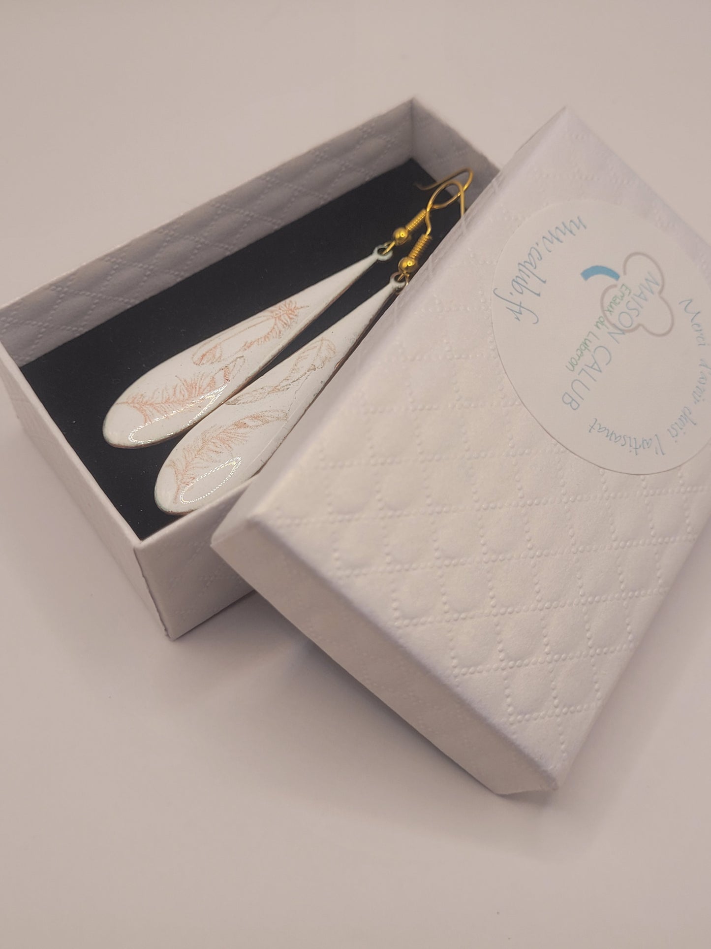 dans leur boite cadeau les boucles d'oreilles gouttes longues en émail sur cuivre aux motifs très fin de plumes . Bijou artisanal maison calub les émaux du Luberon