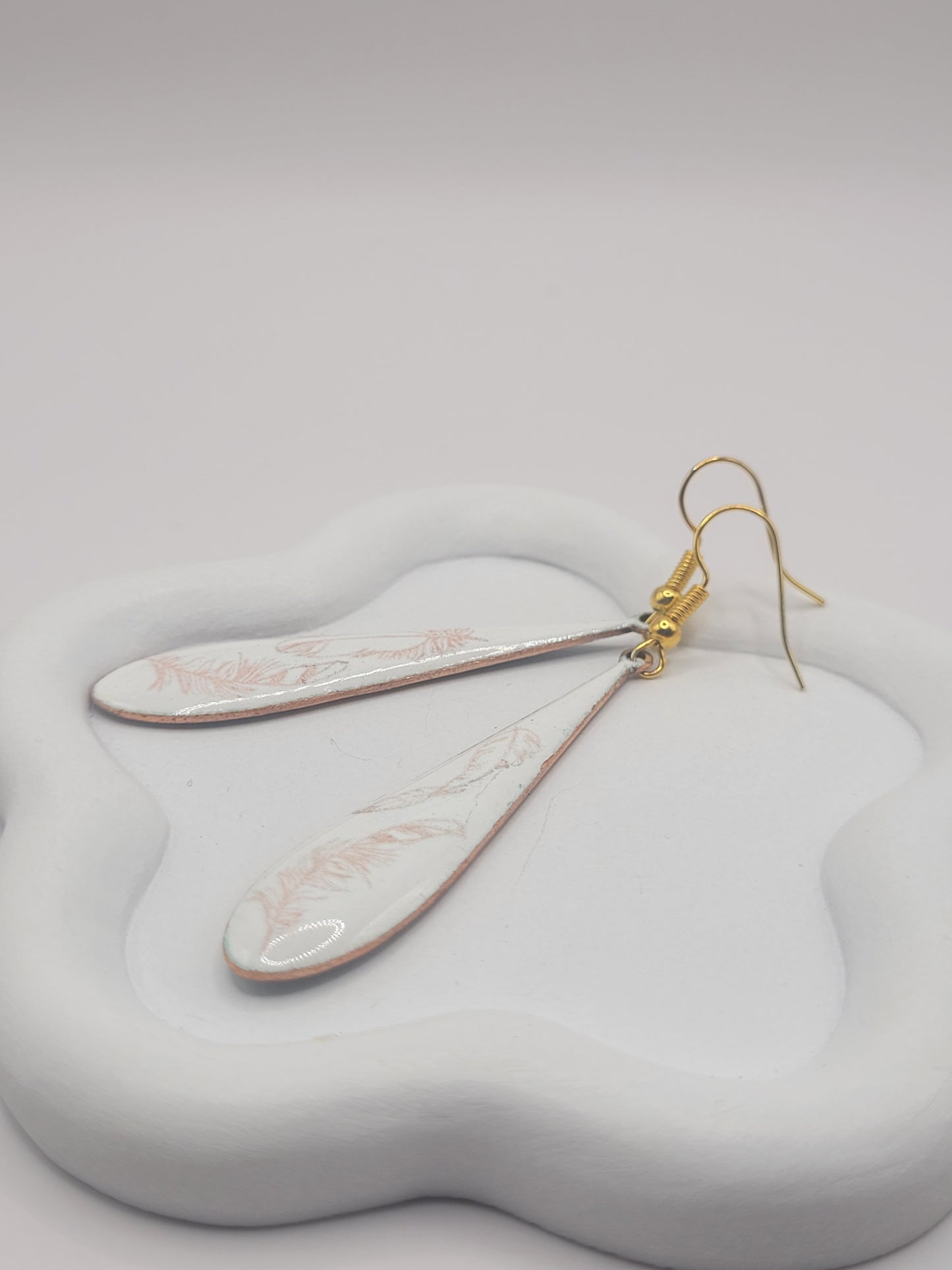gros plan sur les boucles d'oreilles gouttes longues en émail sur cuivre aux motifs très fin de plumes . Bijou artisanal maison calub les émaux du Luberon