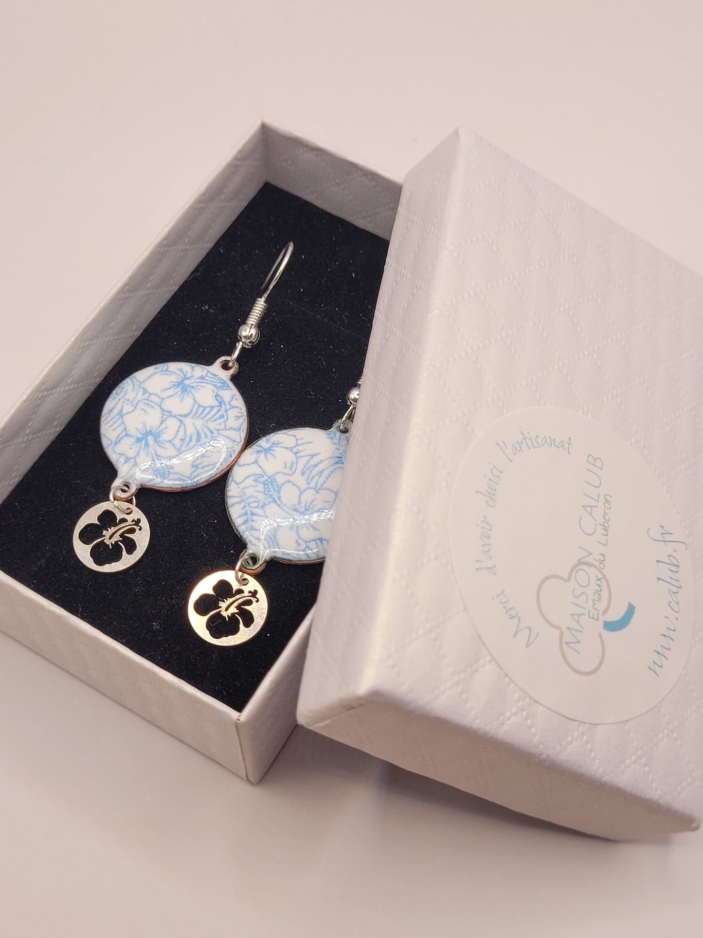 dans leur boite cadeau les boucles d'oreilles en email sur cuivre aux motifs floraux légers hibiscus bleus prolongé par une breloque en argent hibiscus. Bijou artisanal émaillé à la main chez maison CALUB les émaux du Luberon