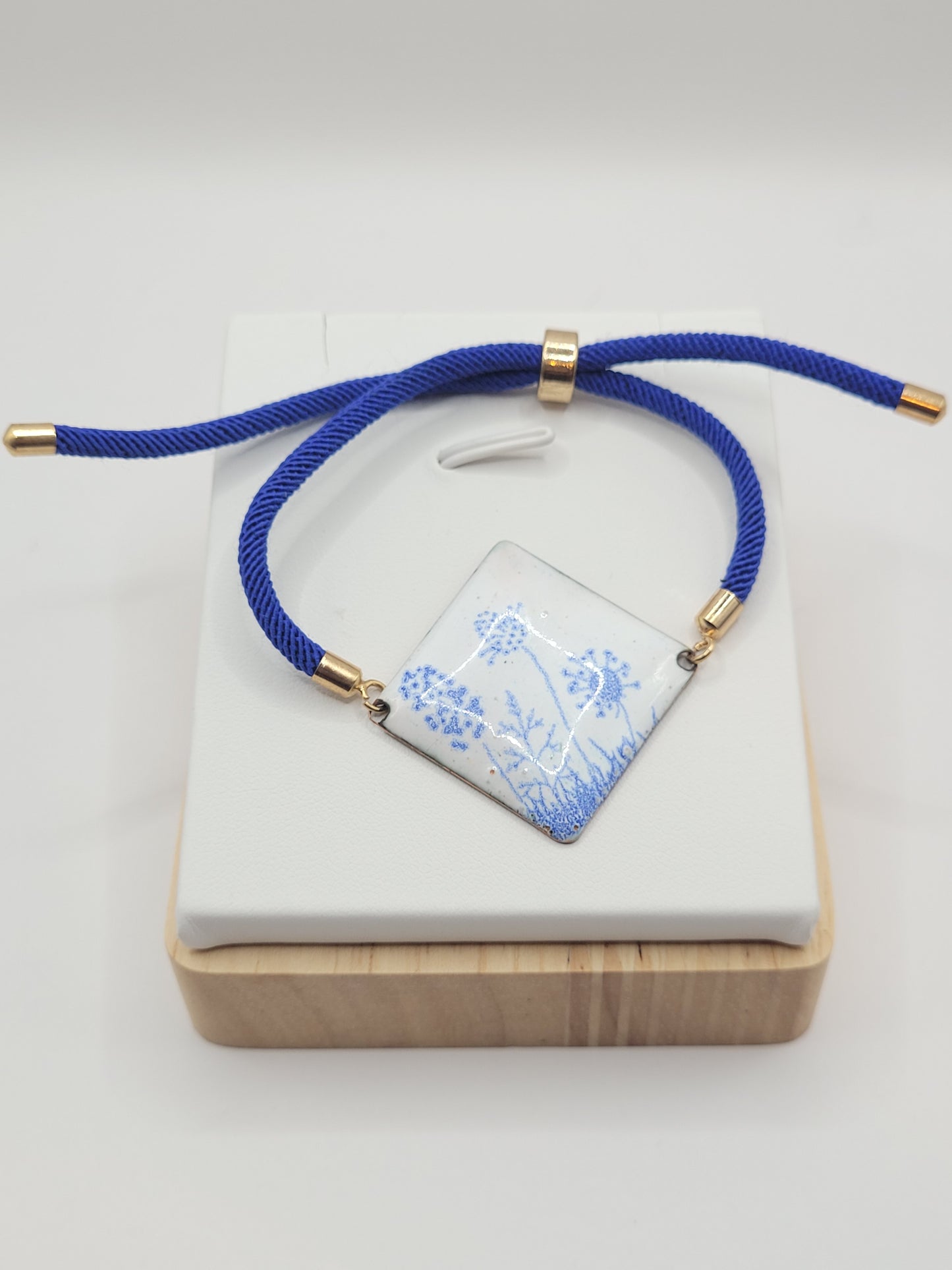 Bracelet cordon en émail sur cuivre de forme carrée. Les motifs bleus sur un émail blanc porcelaine dans la collection Les Uniques chez Maison Calub.
