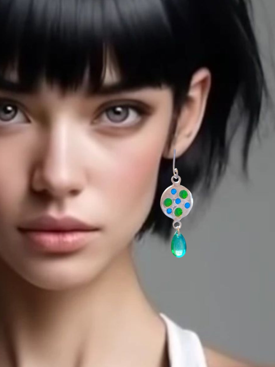 jeune femme brune portant les boucles d'oreilles uniques en émail sur qrgent fin plique-à-jour émaux translucides bleus et vert. Le pendant est prolongé par une perle de verre verte. Bijou artisanal made in France dans les ateliers du Luberon Maison Calub en Provence