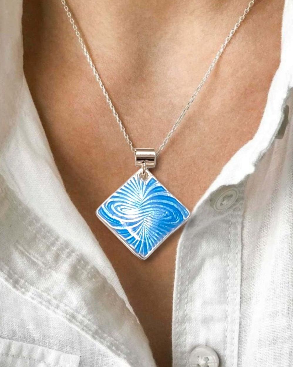 femme portant le Pendentif basse-taille en émail sur argent fin motif symbolique infini contemporain. Bijou artisanal réalisé à la main chez maison Calub les émaux du Luberon. Email translucide bleu