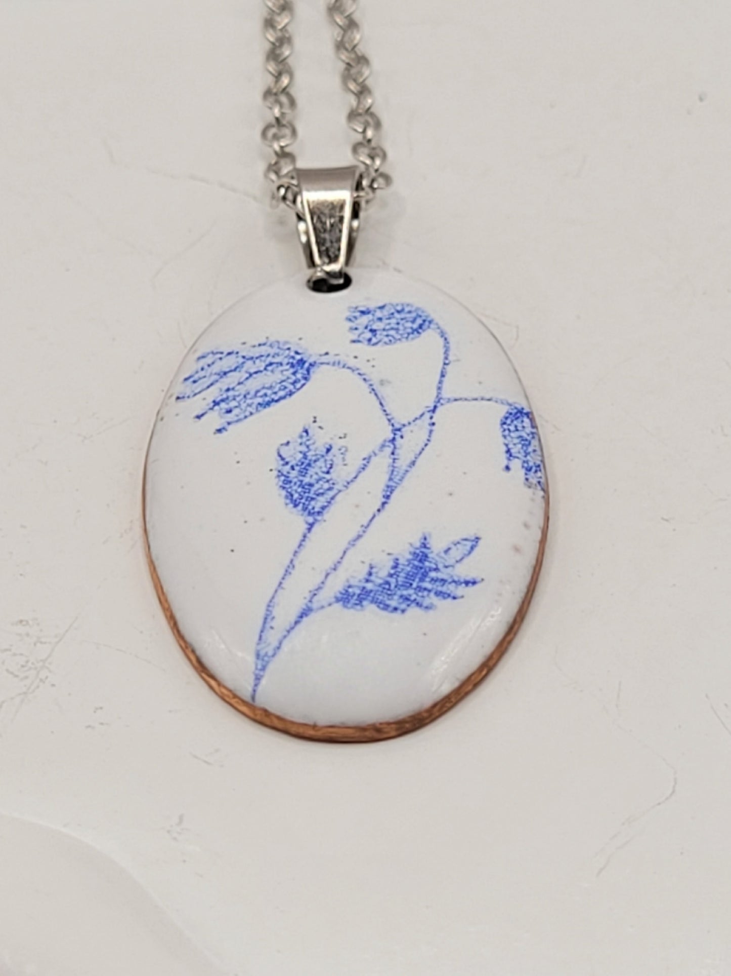 pendentif de la série porcelaine chez maison Calub. Pendentif ovale en émail sur cuivre blanc porcelaine orné de fins motif floraux bleus, monté sur une fine chaine en acier.