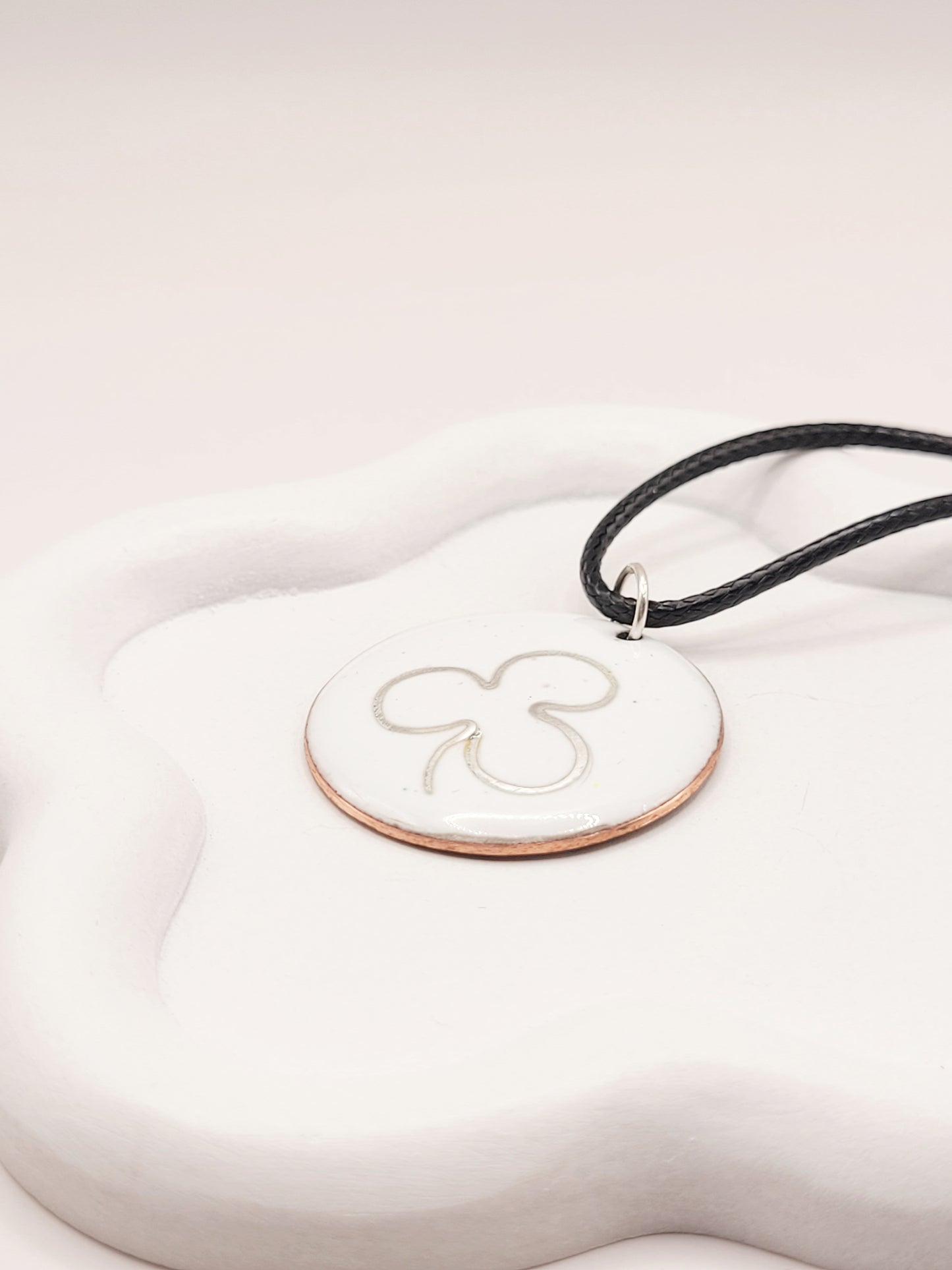 gros plan sur le pendentif en email sur cuivre embleme de maison calub simple trefle en argent fin sur emaux creme effet céramique