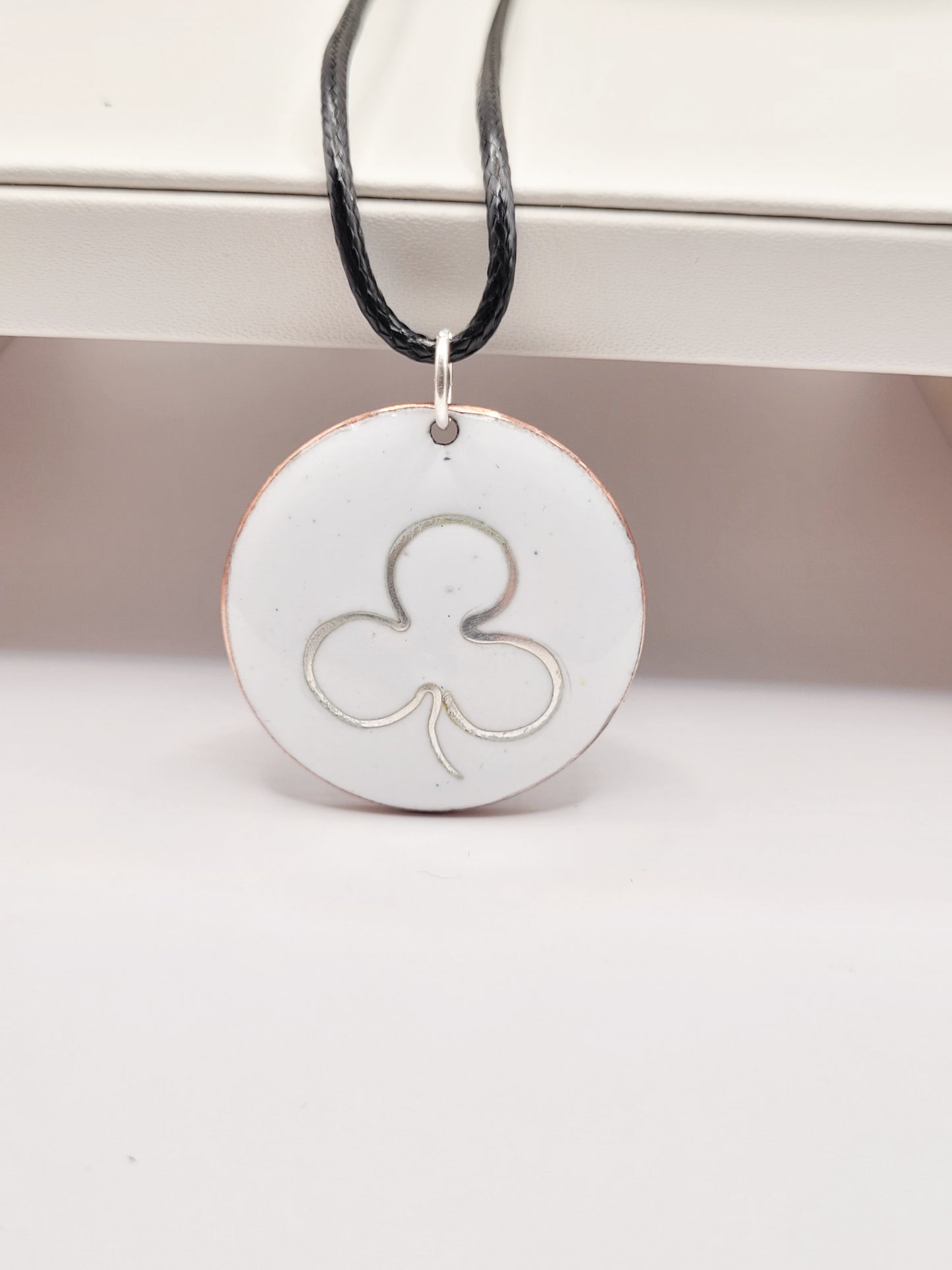 mise en lumière sur le pendentif en email sur cuivre embleme de maison calub simple trefle en argent fin sur emaux creme effet céramique