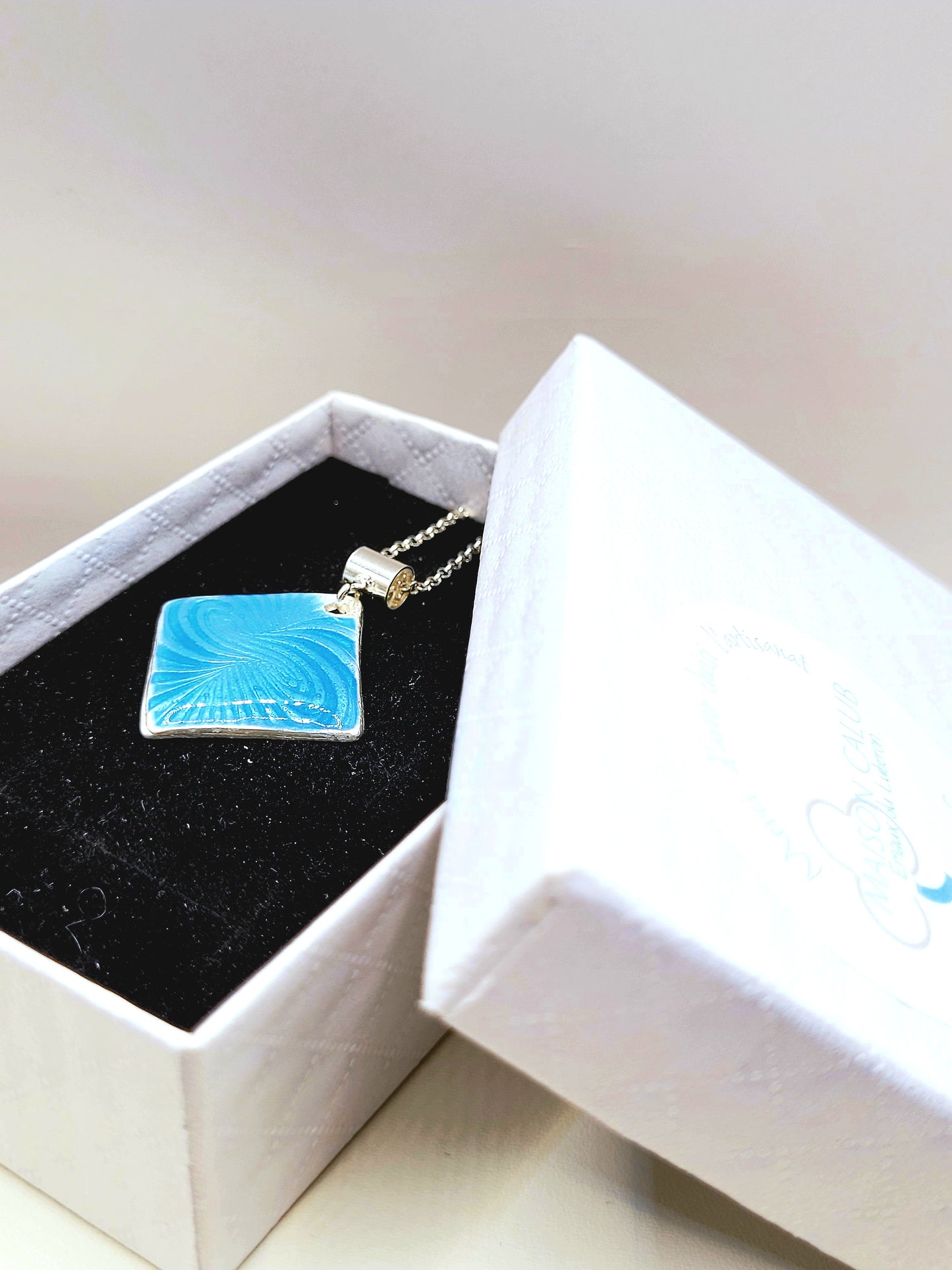 dans sa boite cadeau le Pendentif basse-taille en émail sur argent fin motif symbolique infini contemporain. Bijou artisanal réalisé à la main chez maison Calub les émaux du Luberon. Email translucide bleu