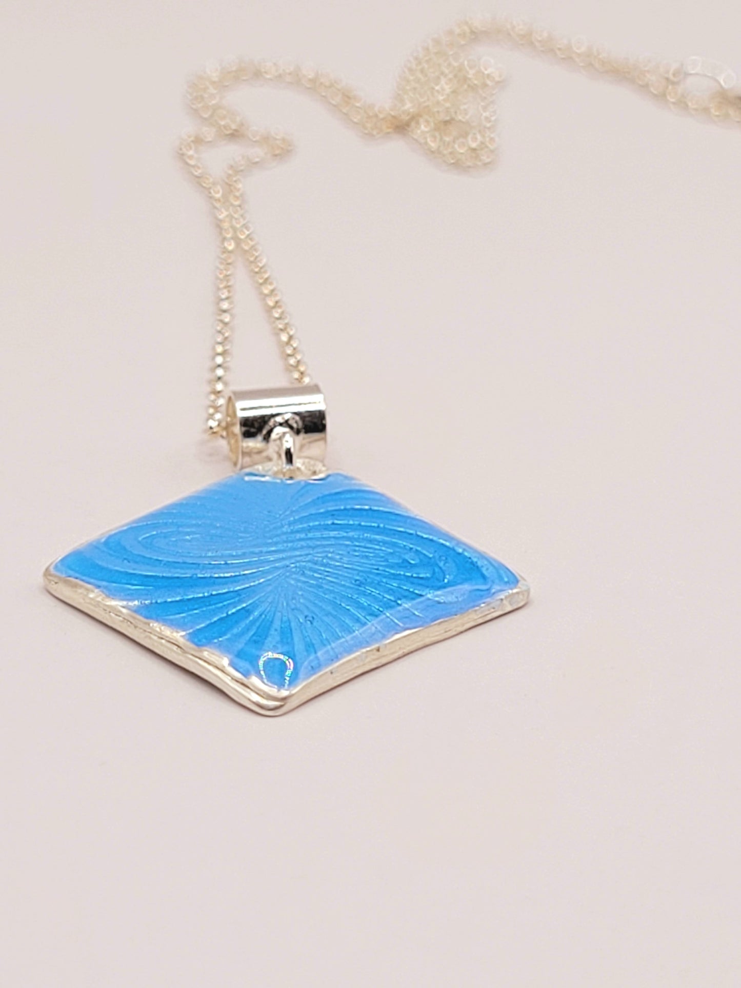 gros plansur Pendentif basse-taille en émail sur argent fin motif symbolique infini contemporain. Bijou artisanal réalisé à la main chez maison Calub les émaux du Luberon. Email translucide bleu
