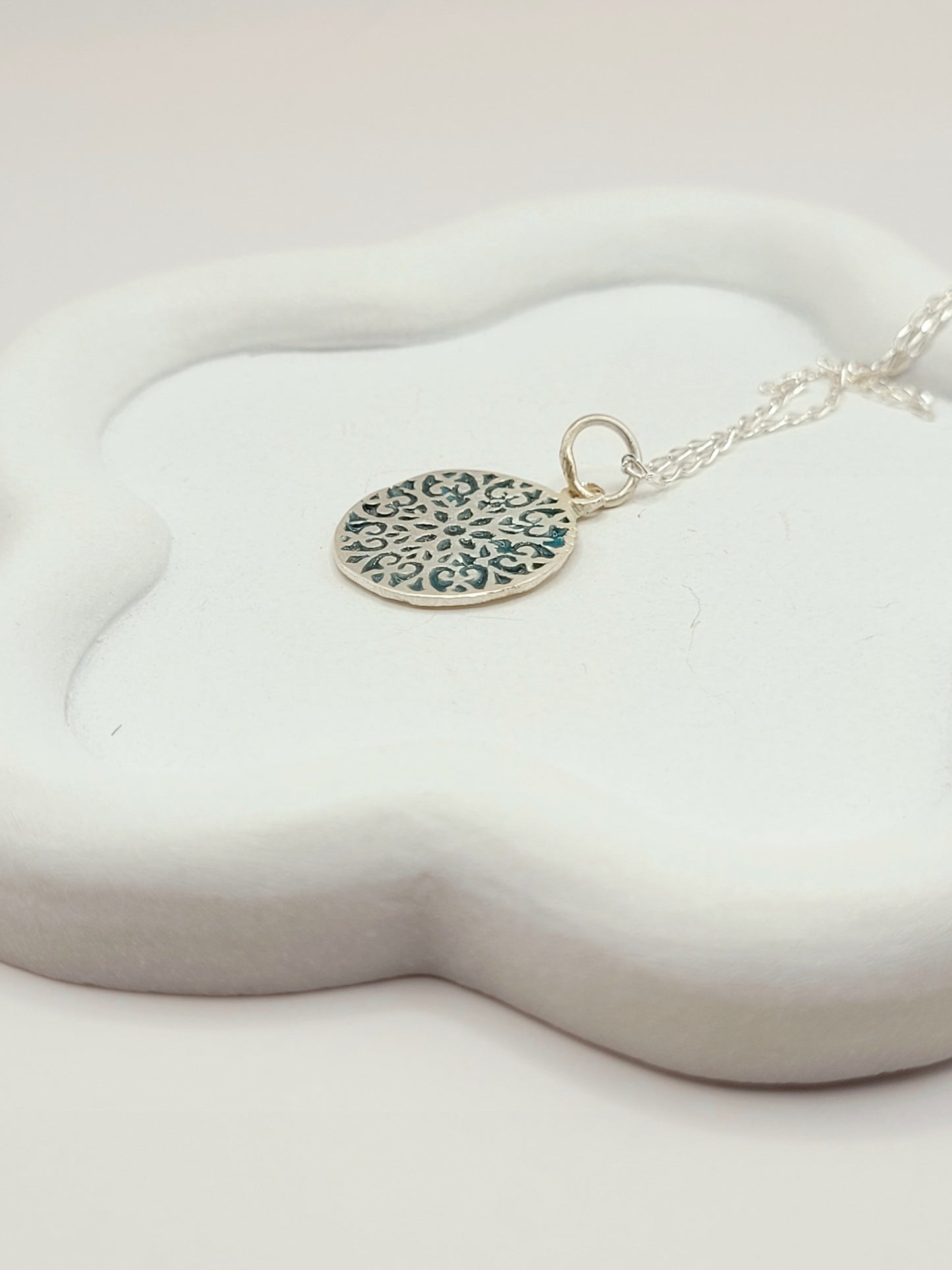 gros plan sur petit pendentif discret en forme de rosace en email sur argent fin bleu. Emaux translucide bijou artisanal réalisé à la main atelier maison calub les émaux du Lubero en Provence made in France