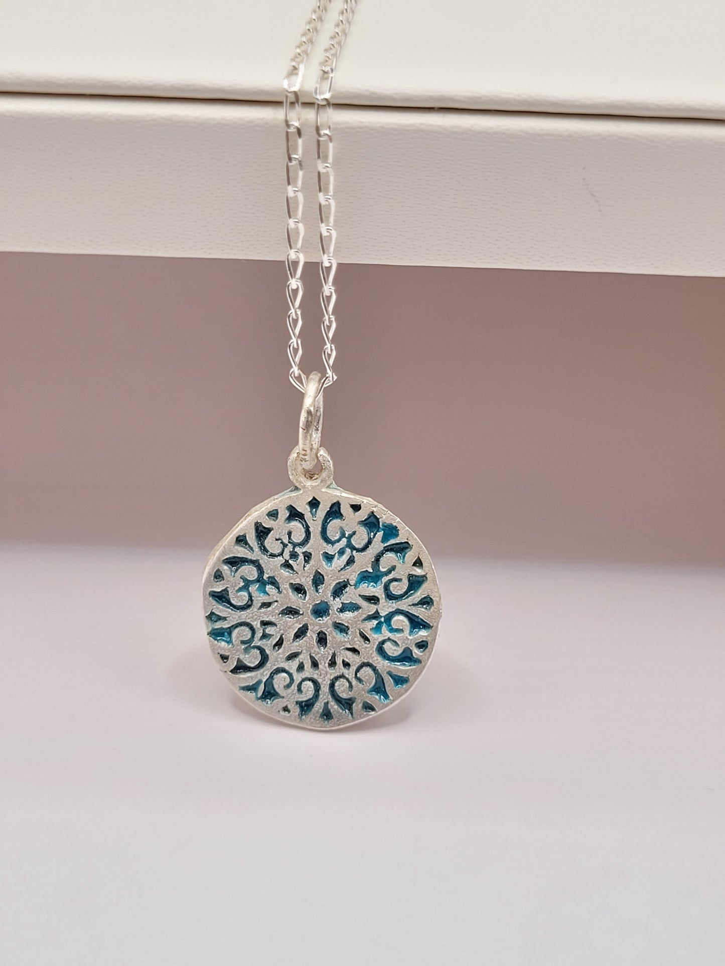 présentation du petit pendentif discret en forme de rosace en champlevé et email sur argent fin bleu. Emaux translucide bijou artisanal réalisé à la main atelier maison calub les émaux du Lubero en Provence made in France