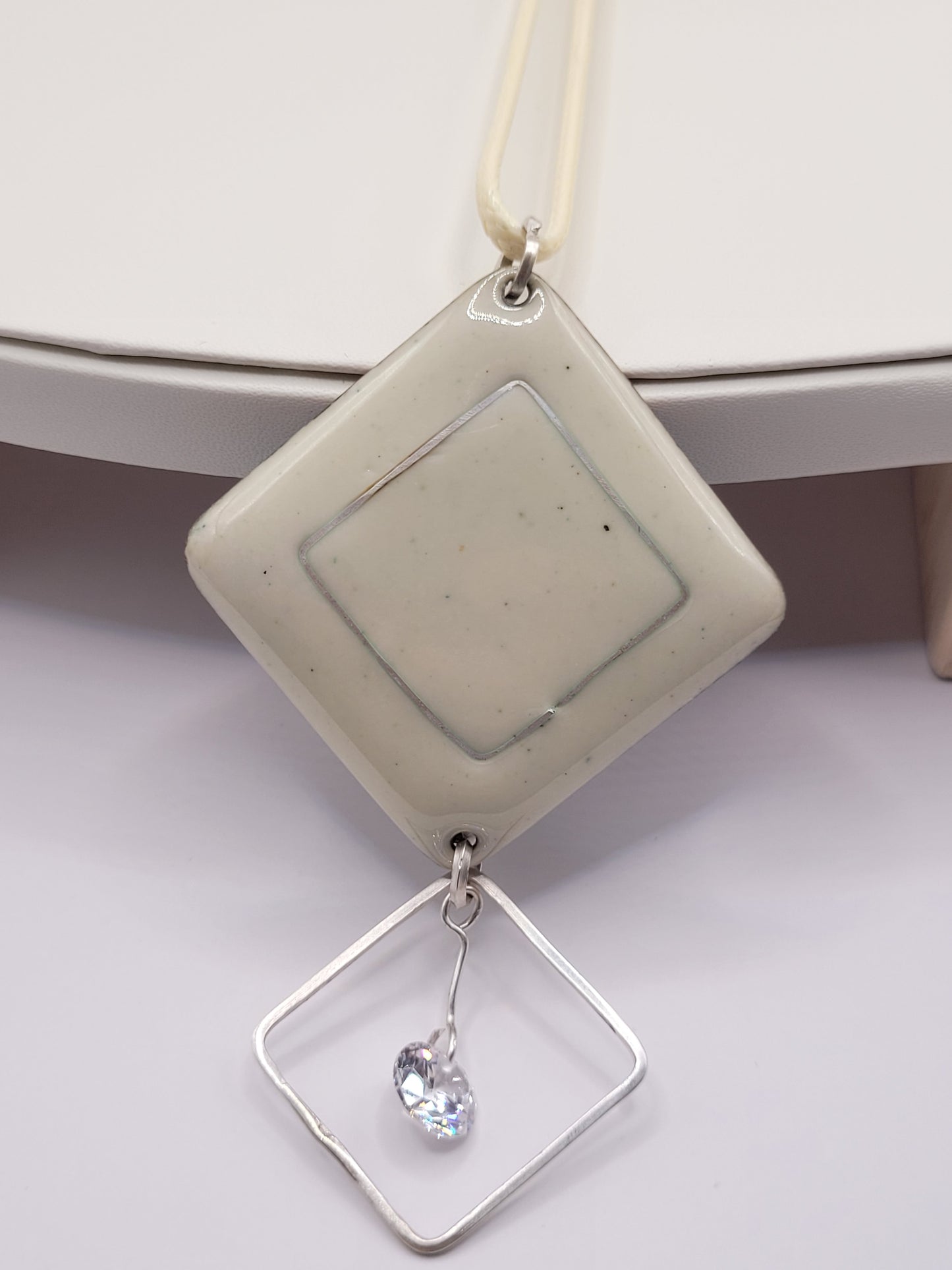 grand pendentif en email sur cuivre clair effet céramique avec l'incrustation d'une ligne d'argent, et breloque aerienne en argent avec zircon sur présentoir