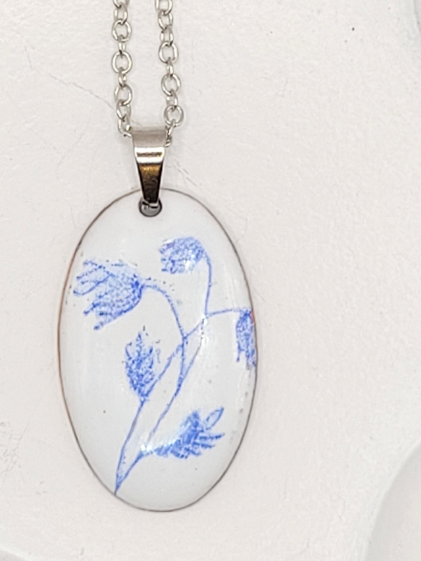 pendentif de la série porcelaine chez maison Calub. Pendentif ovale en émail sur cuivre blanc porcelaine orné de fins motif floraux bleus, monté sur une fine chaine en acier.