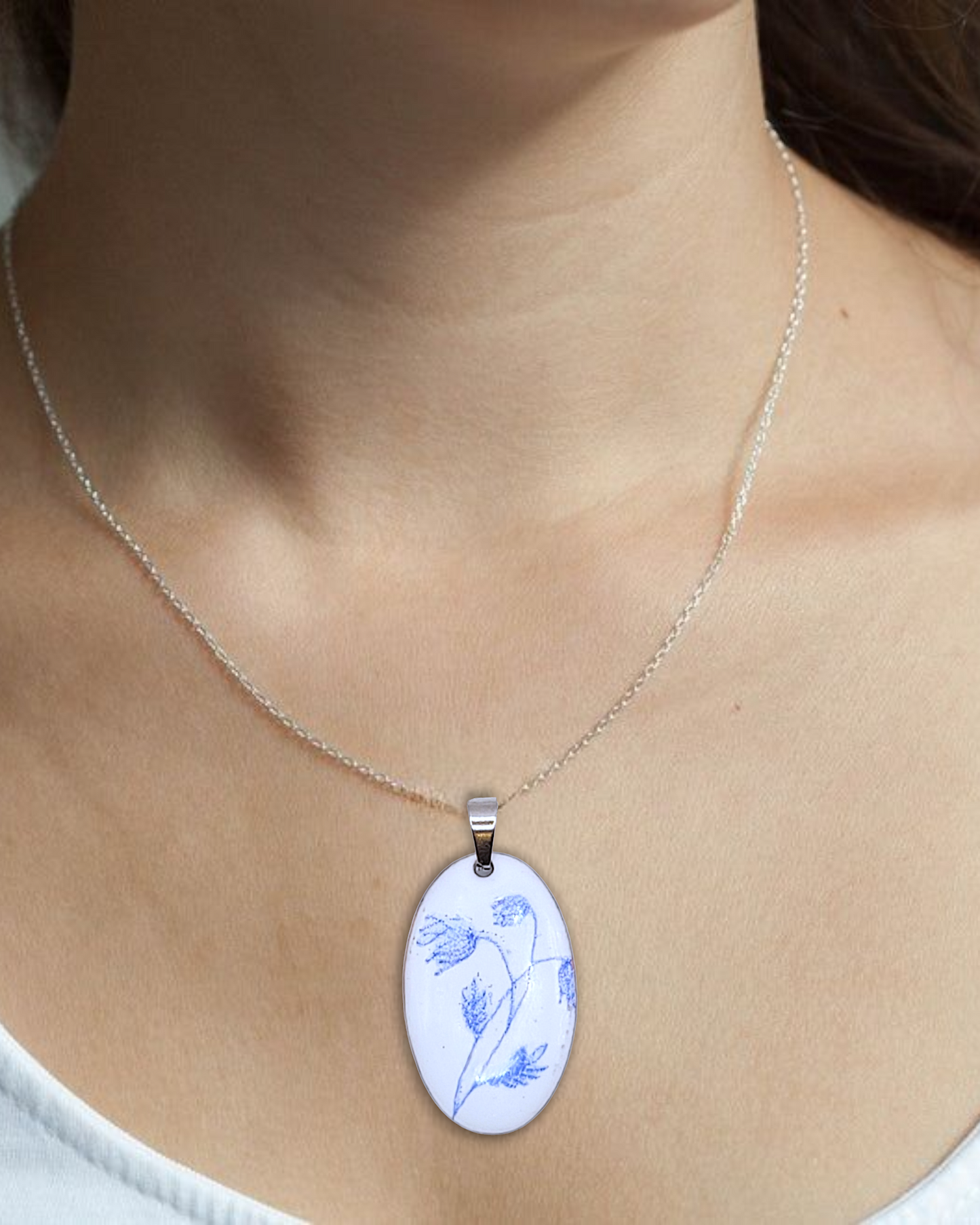 pendentif ovale de la série porcelaine chez maison Calub. Pendentif ovale en émail sur cuivre blanc porcelaine orné de fins motif floraux bleus, monté sur une fine chaine en acier.