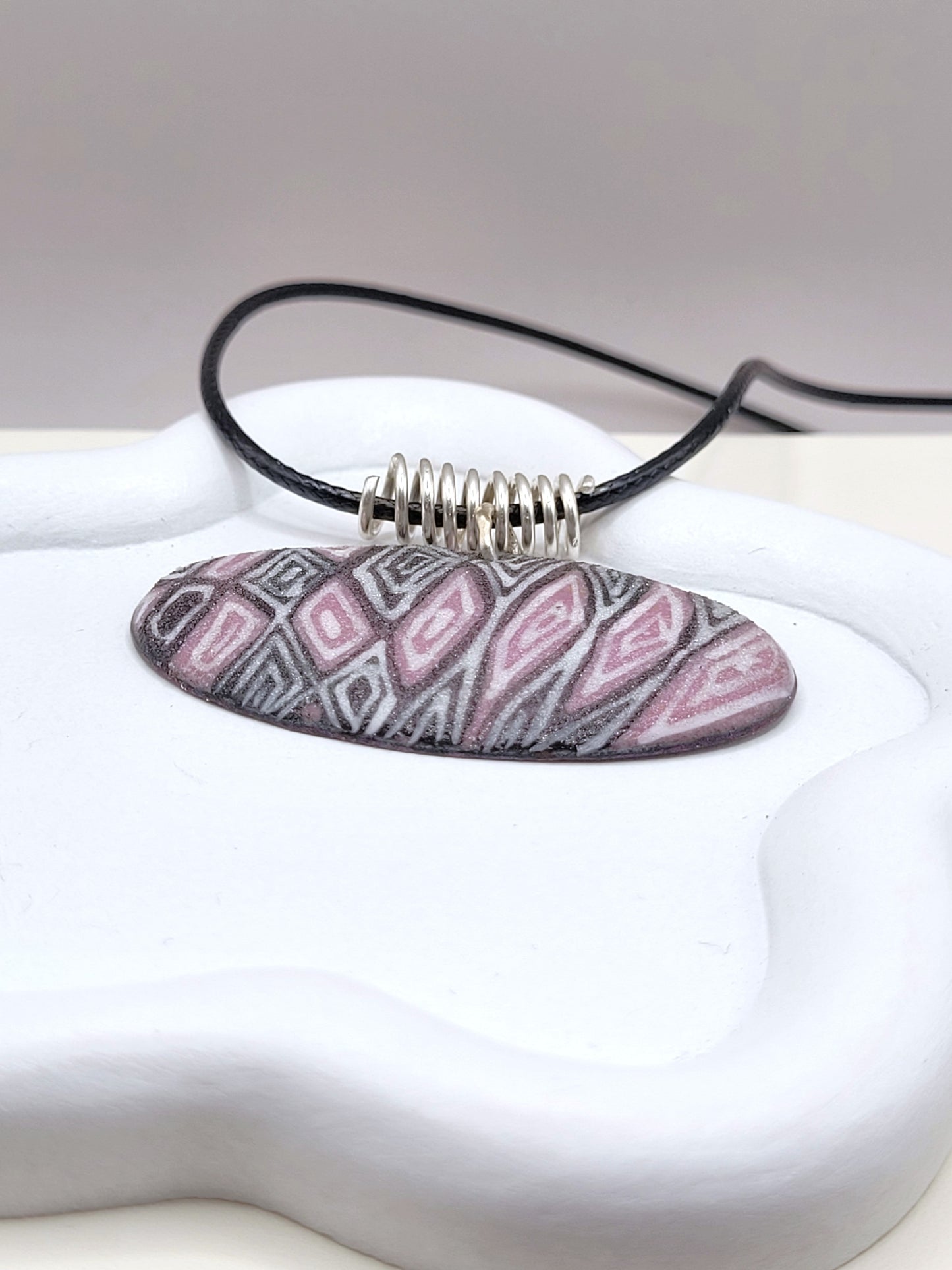 gros plan sur le pendentif ovale au design original inspiré par la lavande de provence chez maison calub émail sur cuivre opaque finition givrée mate émaux traditionnels fait à la main en provence belière en argent monté sur cordon