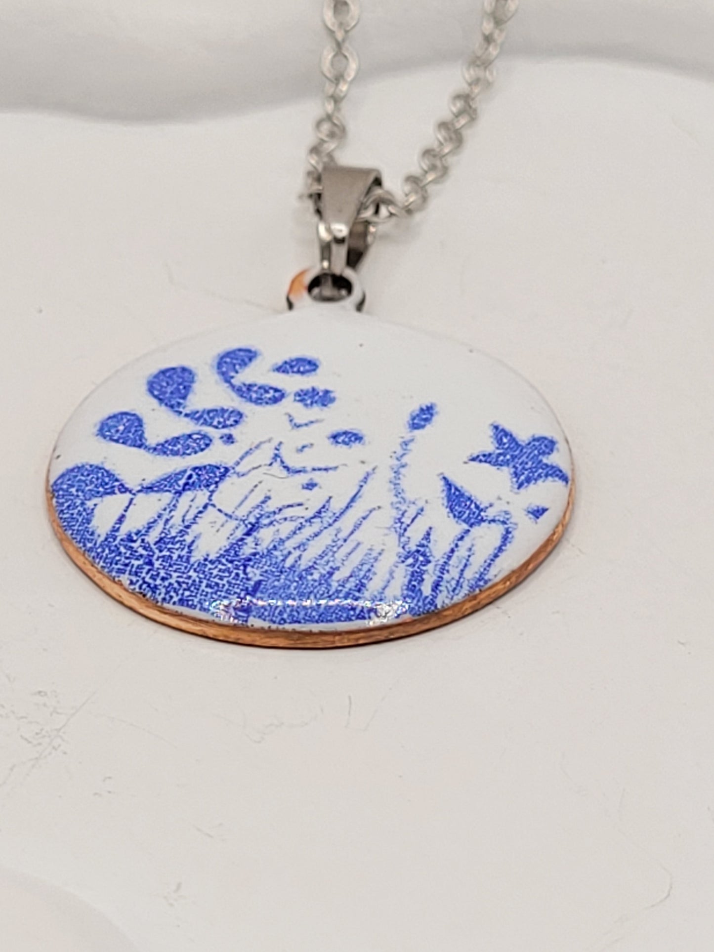 pendentif de la série porcelaine chez maison Calub. Pendentif rond en émail sur cuivre blanc porcelaine orné de fins motif floraux bleus, monté sur une fine chaine en acier.