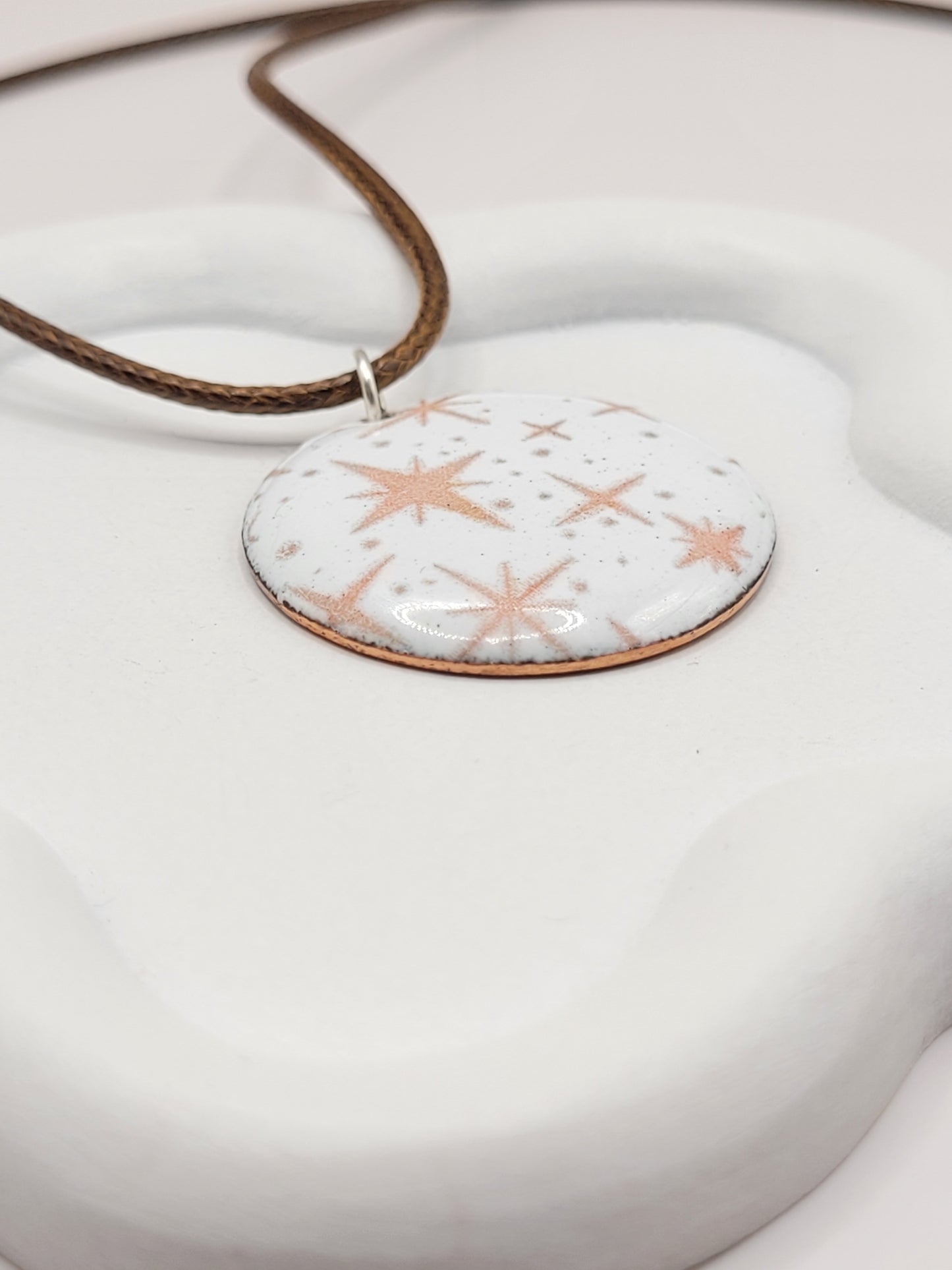 gros plan sur pendentif émaillé lumineux aux fines étoiles rosées sur fond blanc émaux sur cuivre artisanaux de maison calub