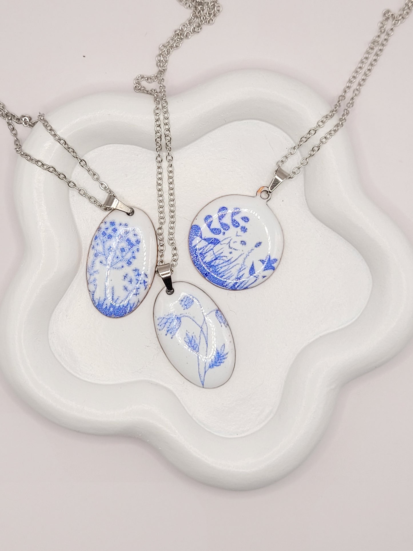 ensemble de 3 pendentifs de la série porcelaine chez maison Calub. Pendentif rond ou ovale en émail sur cuivre blanc porcelaine orné de fins motif floraux bleus, monté sur une fine chaine en acier.