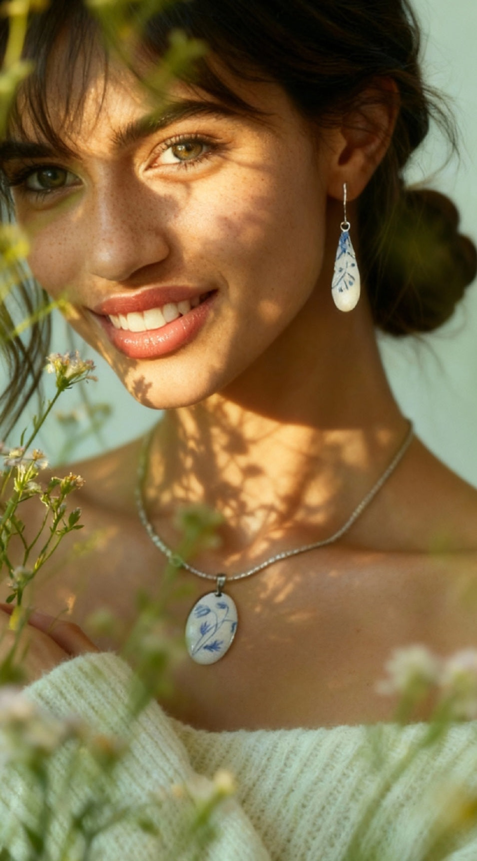 Femme portant un pendentif de la série porcelaine chez maison Calub. Pendentif ovale en émail sur cuivre blanc porcelaine orné de fins motif floraux bleus, monté sur une fine chaine en acier.