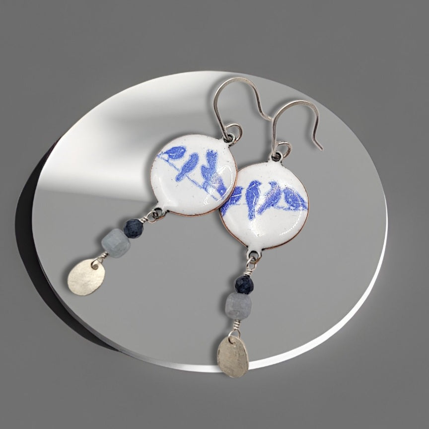 gros plan sur des boucles d'oreilles en émail grand sur sur cuivre, aux motifs fins d'oiseaux, et prolongée par quelques pierres naturelles et breloque en argent