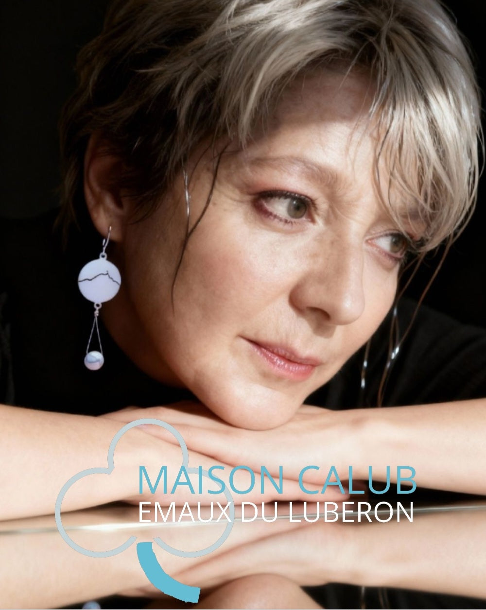 Bijou fait main. femme portant les boucles d'oreilles en émail sur cuivre blanche, ornées de la ligne noire évoquant la montagne sainte-victoire à Aix en Provence. Création maison Calub. Bijou artisanal