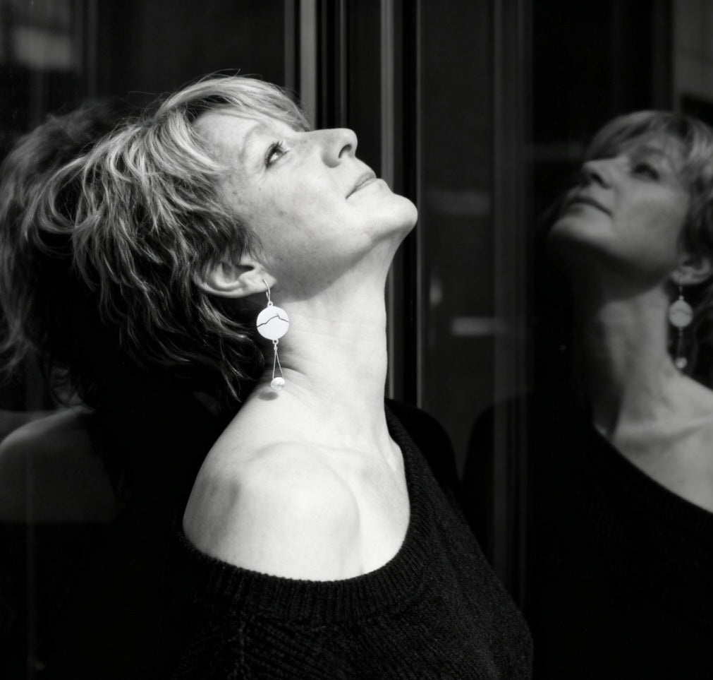 femme portant les boucles d'oreilles en émail sur cuivre blanche, ornées de la ligne noire évoquant la montagne sainte-victoire à Aix en Provence. Création maison Calub. Bijou artisanal