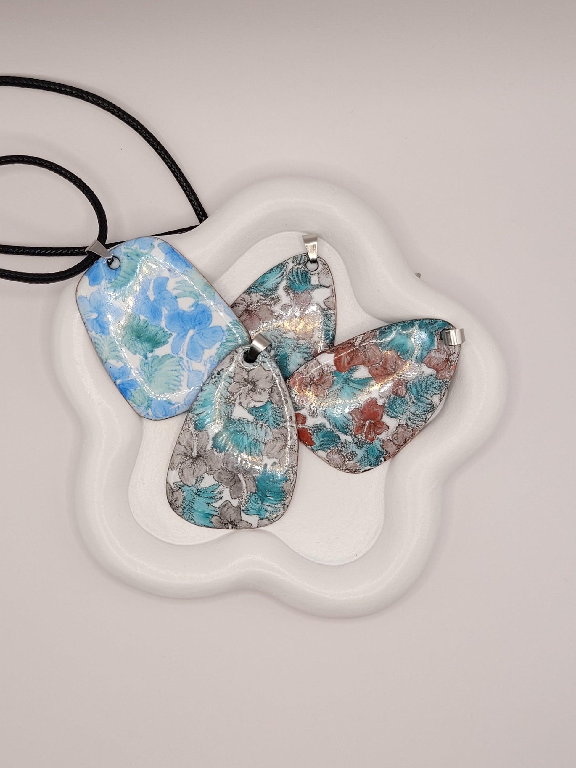 différents pendentifs de la ligne Liberty chez maison CALUB, pendentif en émail peint à la main monté sur un cordon noir, création artisanale originale. Couleurs variées