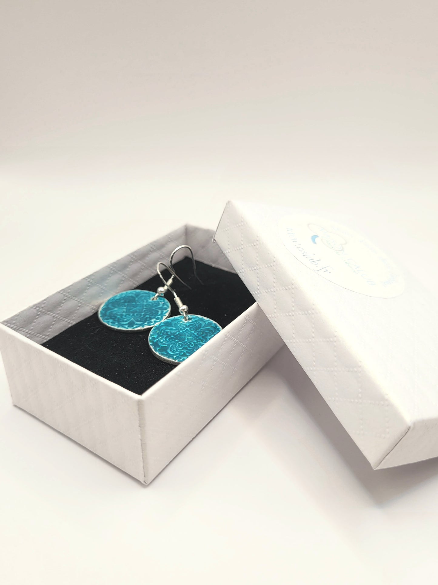 dans une petite boite cadeau les boucles d'oreilles uniques en émail sur argent fin basse-taille de petits motifs et émaux translucides bleus. Bijou artisanal de maison Calub les émaux de Provence Made in France