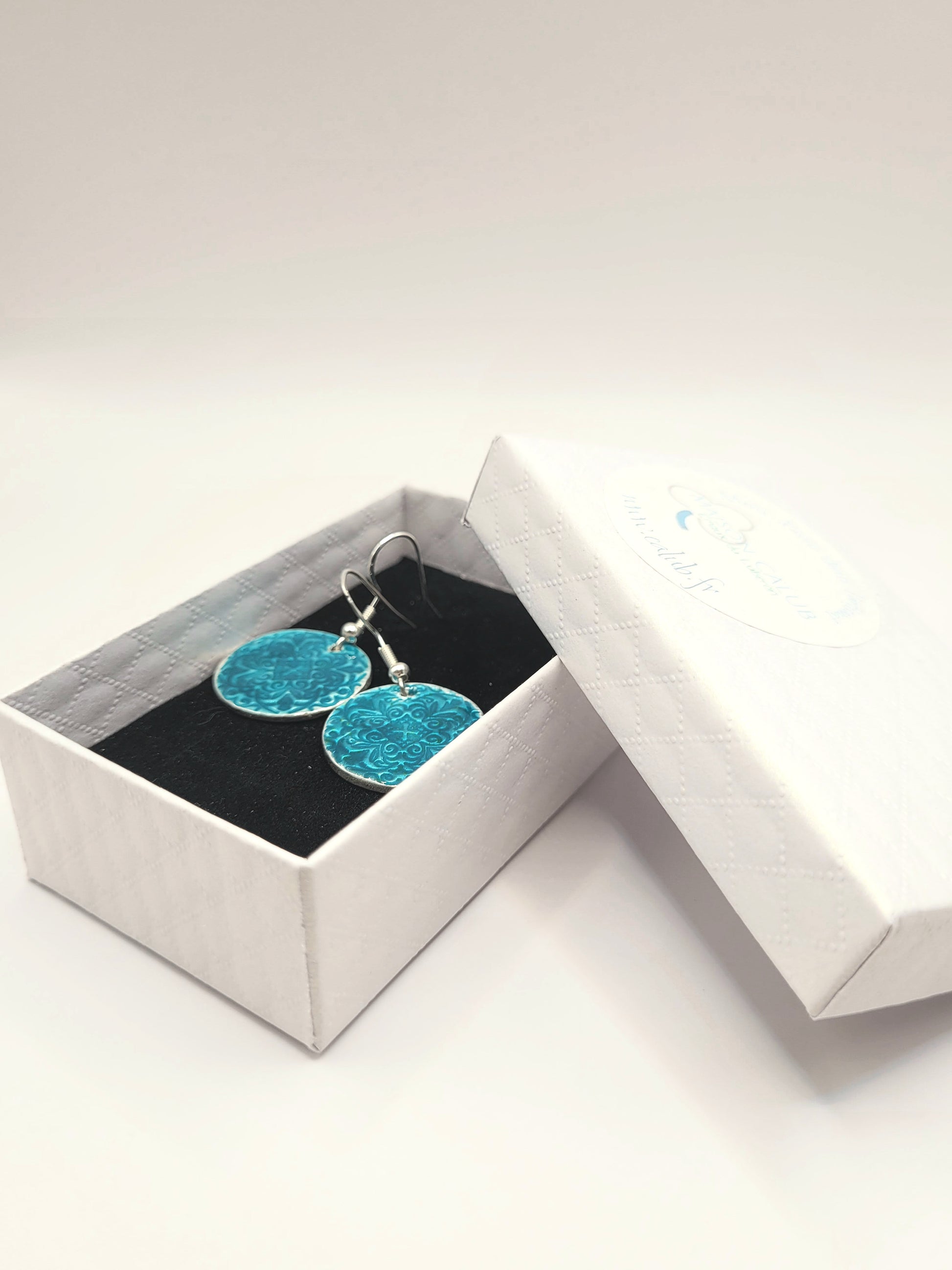 dans une petite boite cadeau les boucles d'oreilles uniques en émail sur argent fin basse-taille de petits motifs et émaux translucides bleus. Bijou artisanal de maison Calub les émaux de Provence Made in France