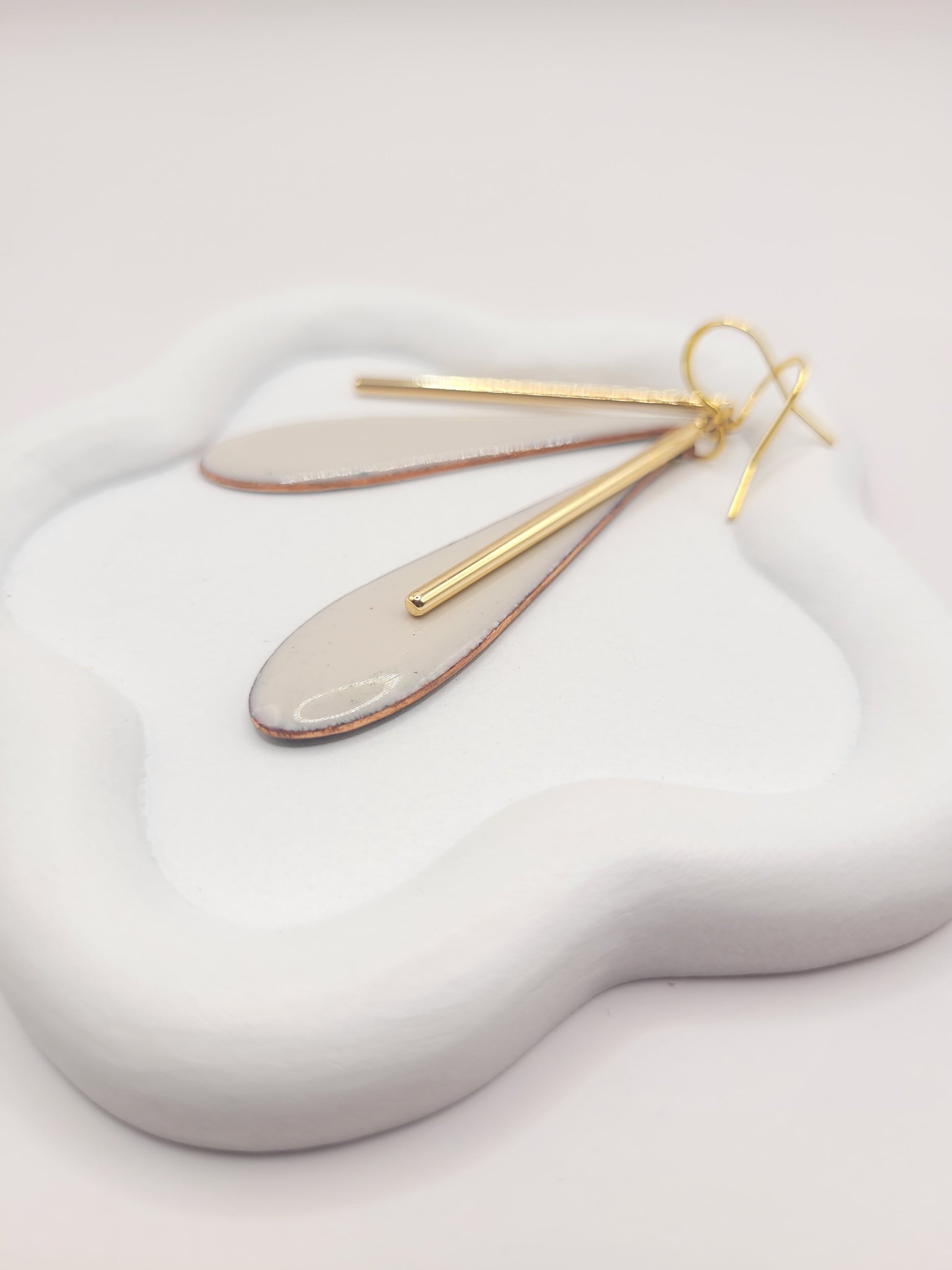 bijou artisanal boucles d'oreilles en email blanc grème et agrémentées d'une longue breloque dorée très simples et légères création maison Calub. Sur un présentoir