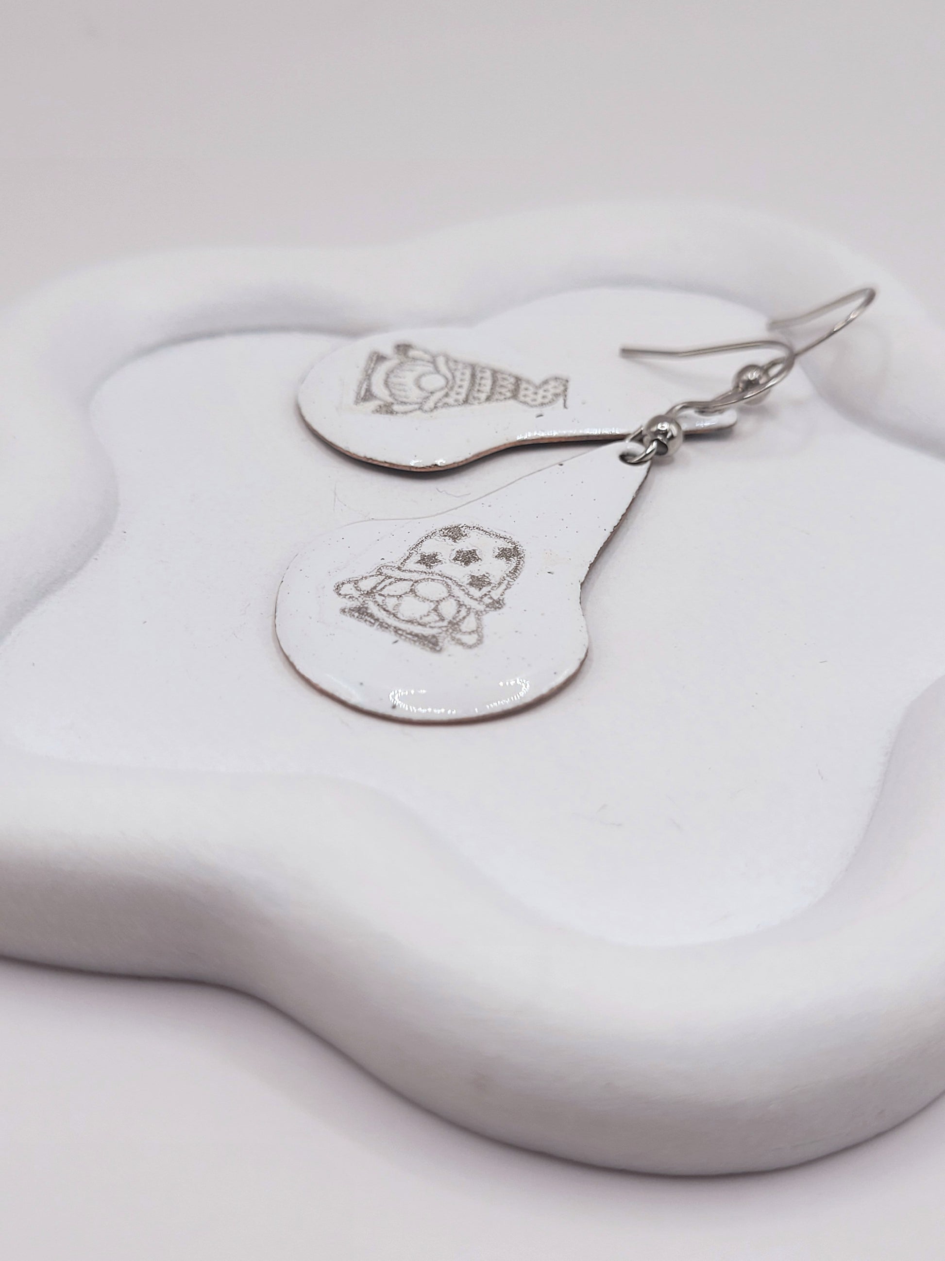 gros plan sur boucles d'oreilles en email sur cuivre en forme de goutte avec un petit personnage mignon noir sur fond blanc maison calub