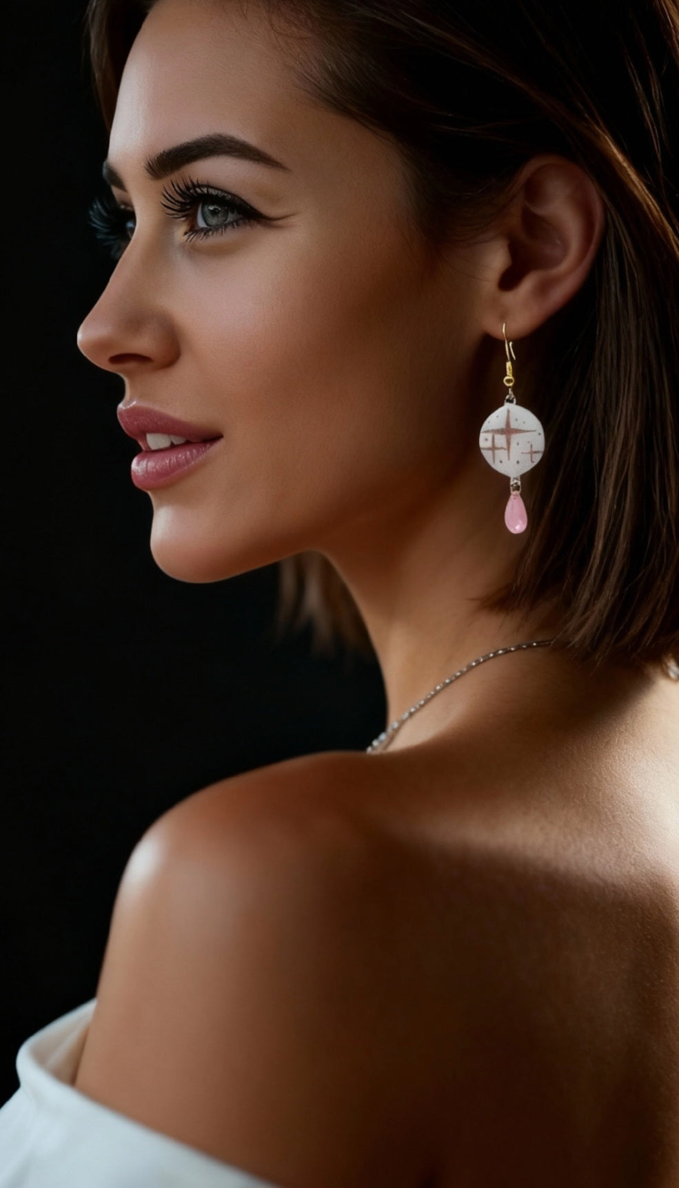 femme portant des boucles d'oreilles en émail sur cuivre aux motif d'étoiles rosés sur blanc prolongé par une perle de verre goutte. Bijou artisanal fait à la main chez maison calub les emaux du Luberon