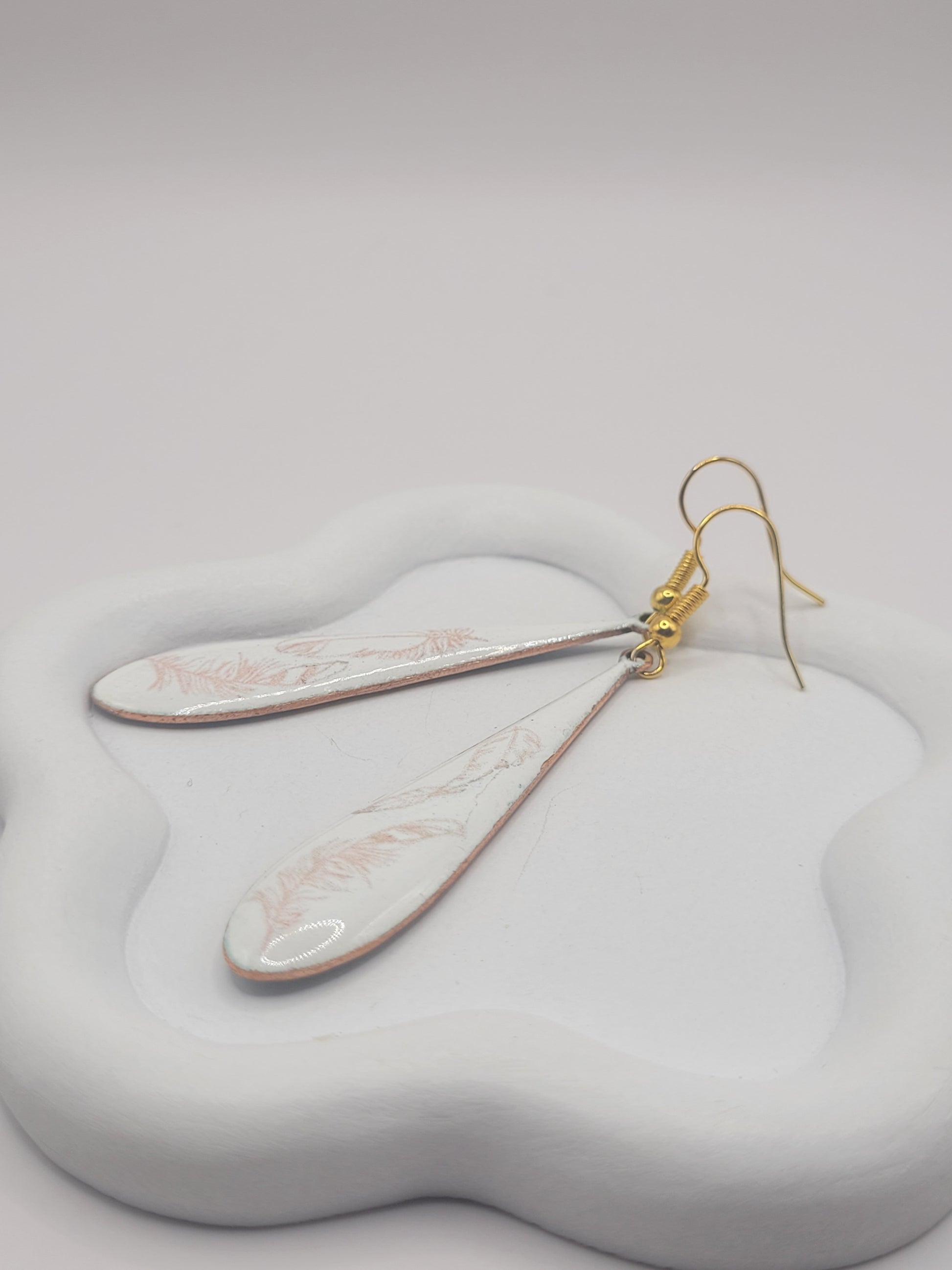 gros plan sur les boucles d'oreilles gouttes longues en émail sur cuivre aux motifs très fin de plumes . Bijou artisanal maison calub les émaux du Luberon