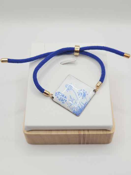 Bracelet cordon en émail sur cuivre de forme carrée. Les motifs bleus sur un émail blanc porcelaine dans la collection Les Uniques chez Maison Calub.
