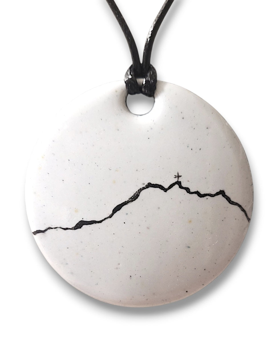 grand pendentif en émail blanc avec une ligne noire représentant le profil de la montagne Sainte-Victoire. Création artisanale Maison calub. Emaux opaques peints à la main. 