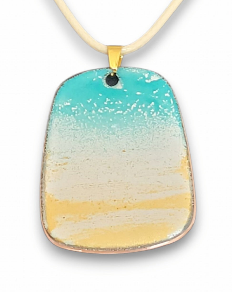 présentation d'un pendentif qui rappelle la plage, en émail sur cuivre et mica. Couleur bleu et doré. Forme trapèze. Création artisanale maison calub