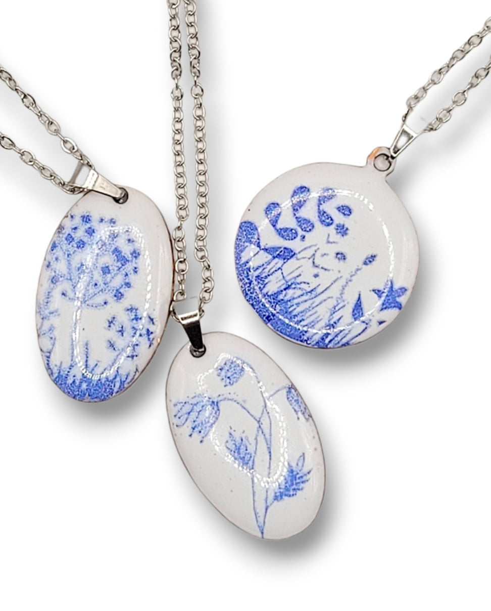 pendentifs de la série porcelaine chez maison Calub.  émail sur cuivre blanc porcelaine orné de fins motif floraux bleus, monté sur une fine chaine en acier. Emaux opaques