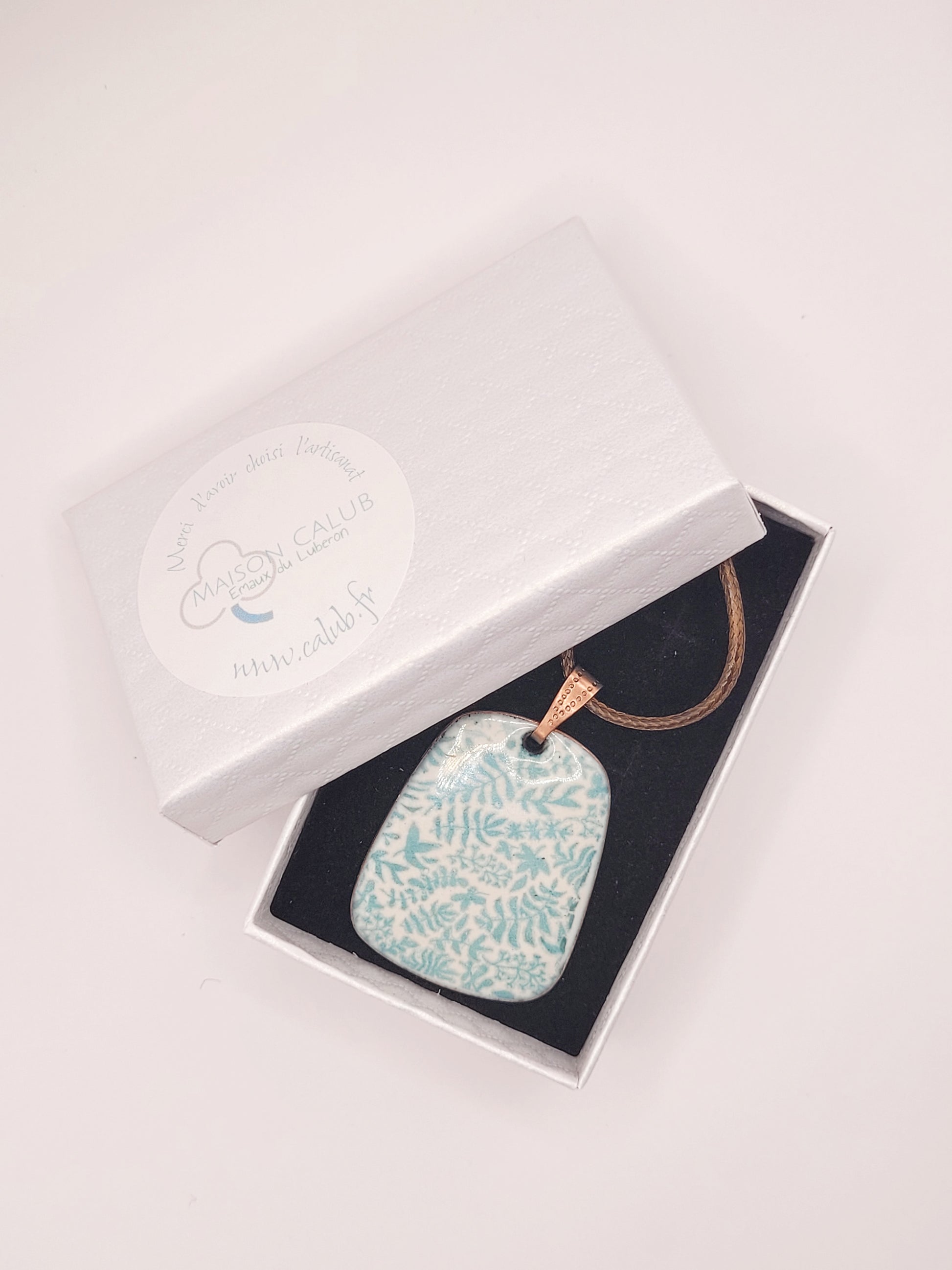 dans une boite cadeau un bijou artisanal pendentif emaux sur cuivre peint à la main motif feuillage vert sur blanc creme de maison calub