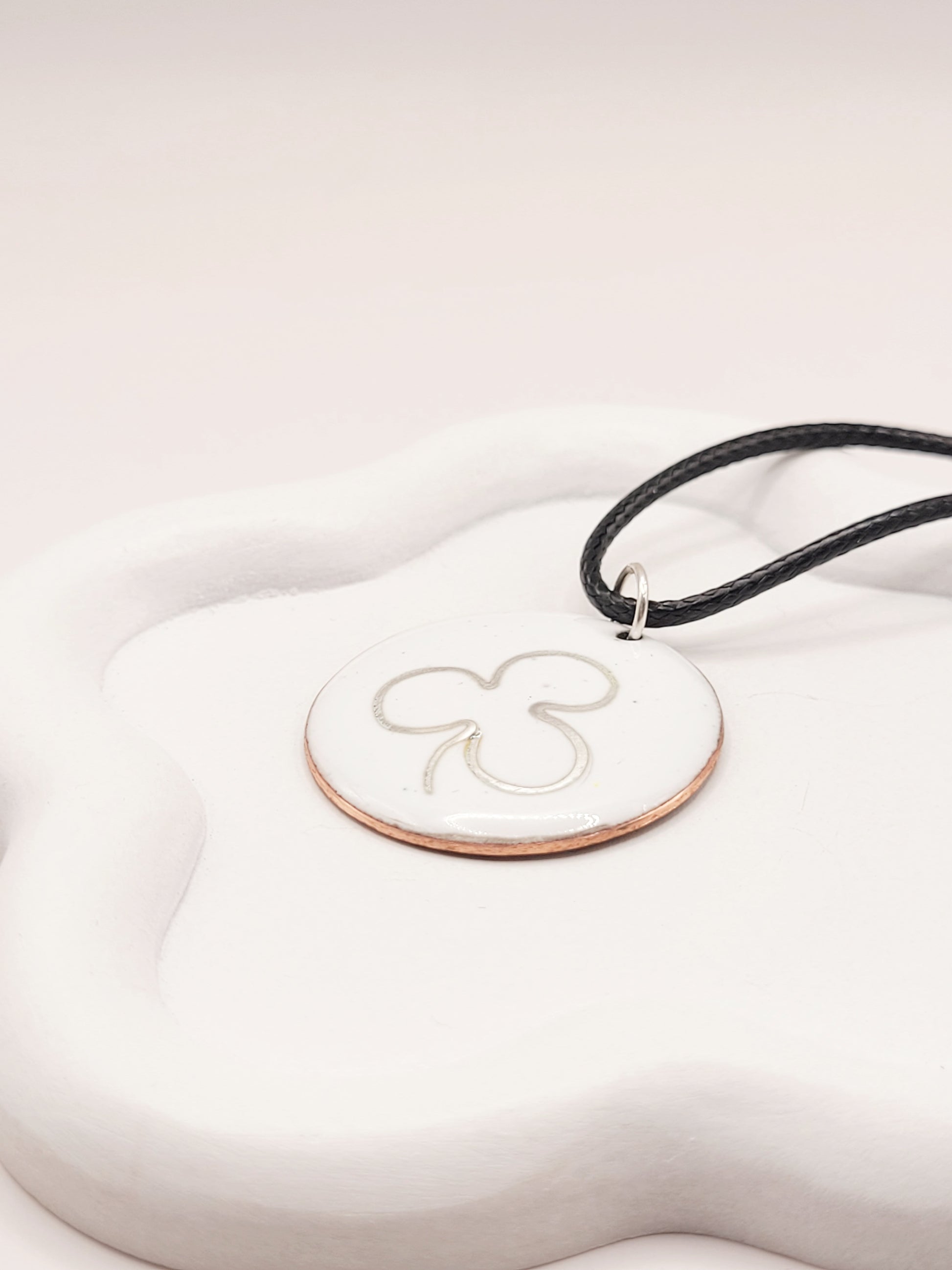 gros plan sur le pendentif en email sur cuivre embleme de maison calub simple trefle en argent fin sur emaux creme effet céramique