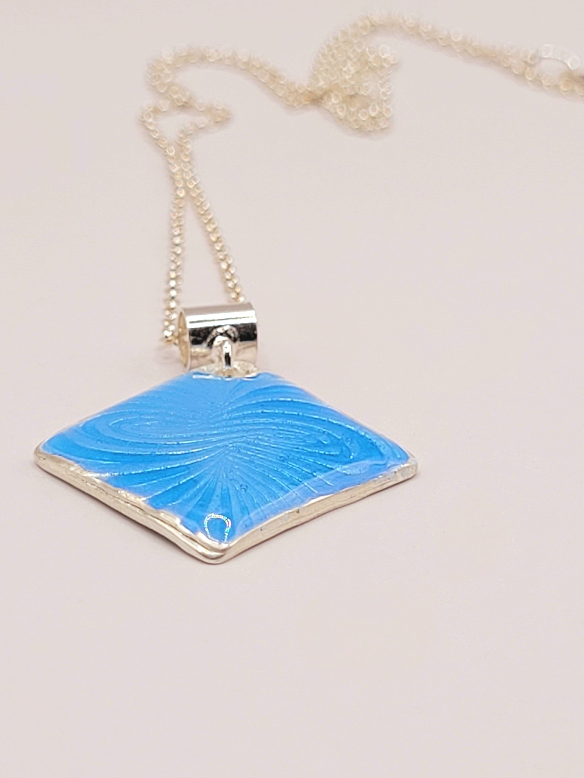 gros plansur Pendentif basse-taille en émail sur argent fin motif symbolique infini contemporain. Bijou artisanal réalisé à la main chez maison Calub les émaux du Luberon. Email translucide bleu