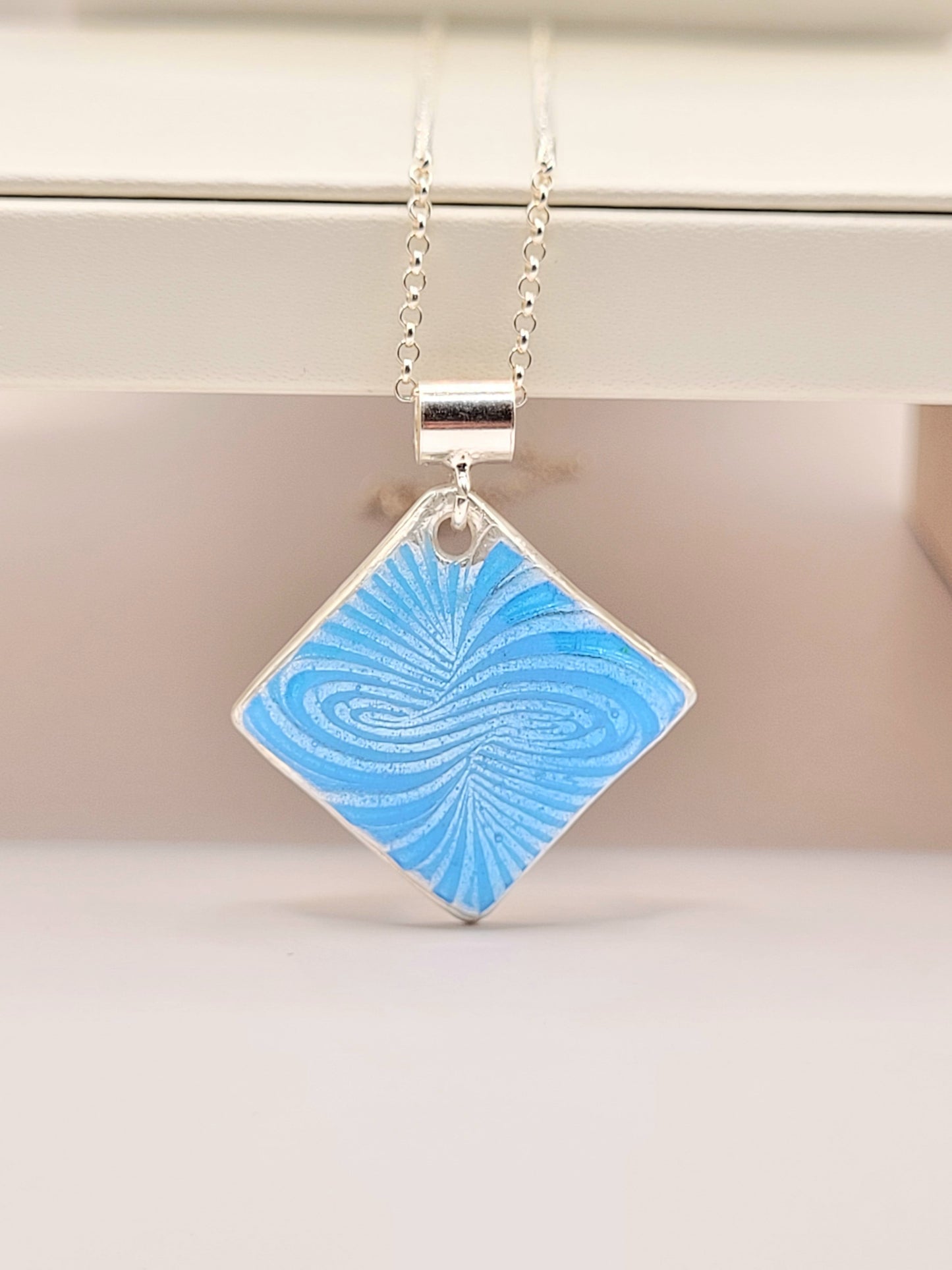 Pendentif basse-taille en émail sur argent fin motif symbolique infini contemporain. Bijou artisanal réalisé à la main chez maison Calub les émaux du Luberon. Email translucide bleu