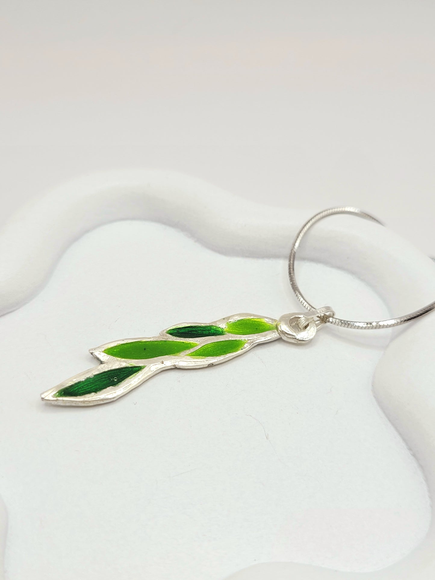gros plan sur le pendentif léger en émail sur cuivre champlevé forme branche de laurier couleur verte 2 tons. Bijou artisanal émaux translucides chez maison calub les émaux du Luberon