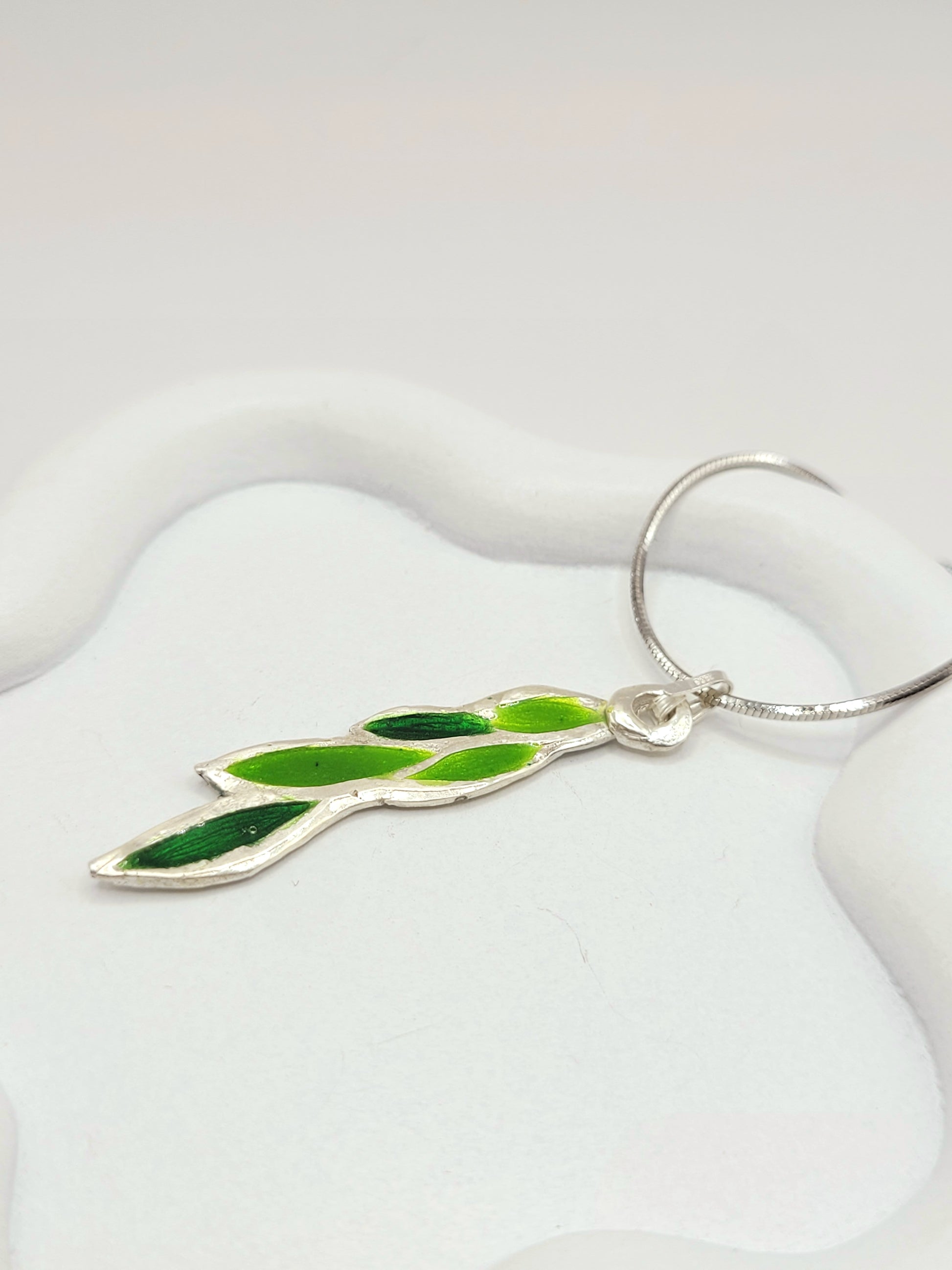 gros plan sur le pendentif léger en émail sur cuivre champlevé forme branche de laurier couleur verte 2 tons. Bijou artisanal émaux translucides chez maison calub les émaux du Luberon