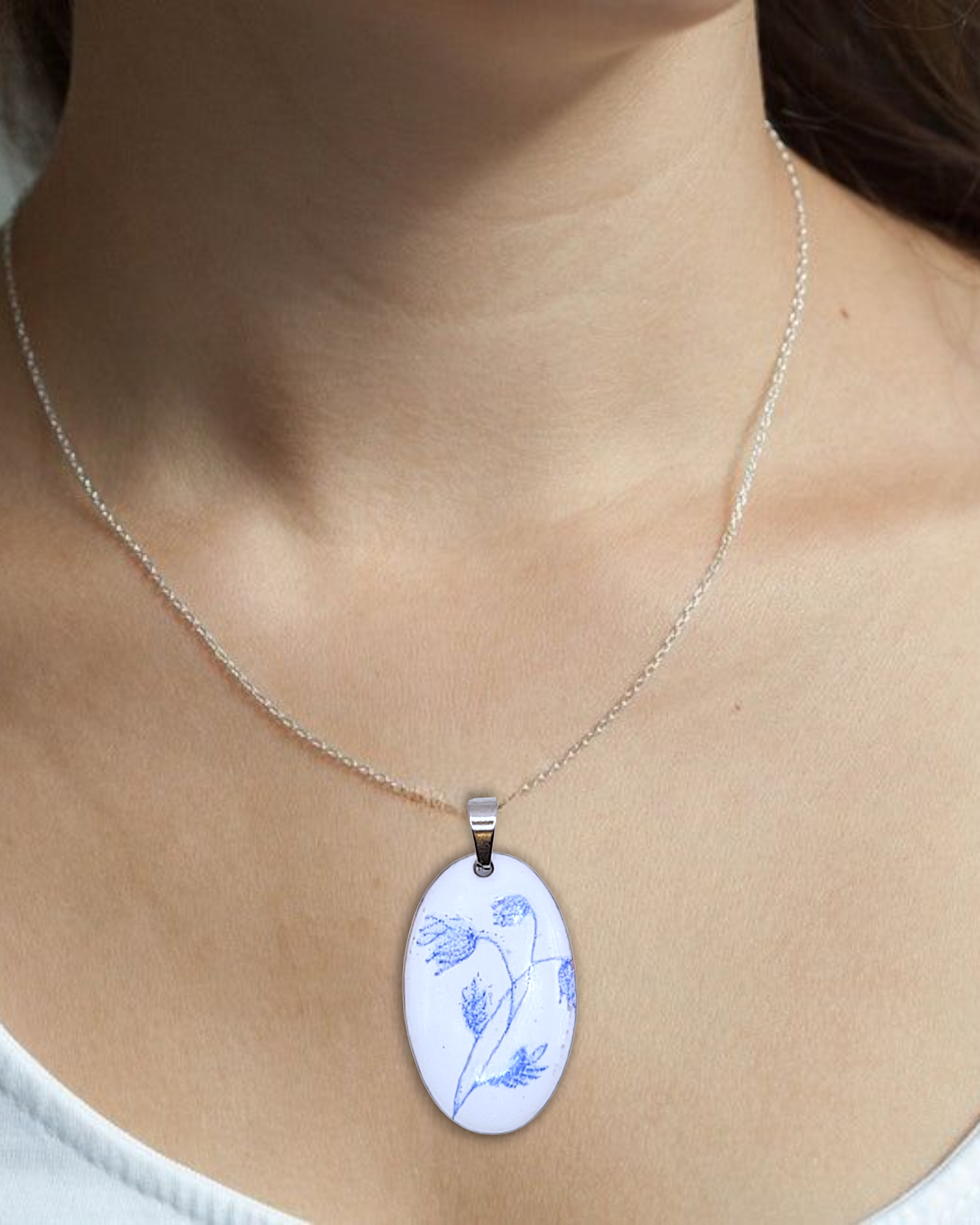 pendentif ovale de la série porcelaine chez maison Calub. Pendentif ovale en émail sur cuivre blanc porcelaine orné de fins motif floraux bleus, monté sur une fine chaine en acier.