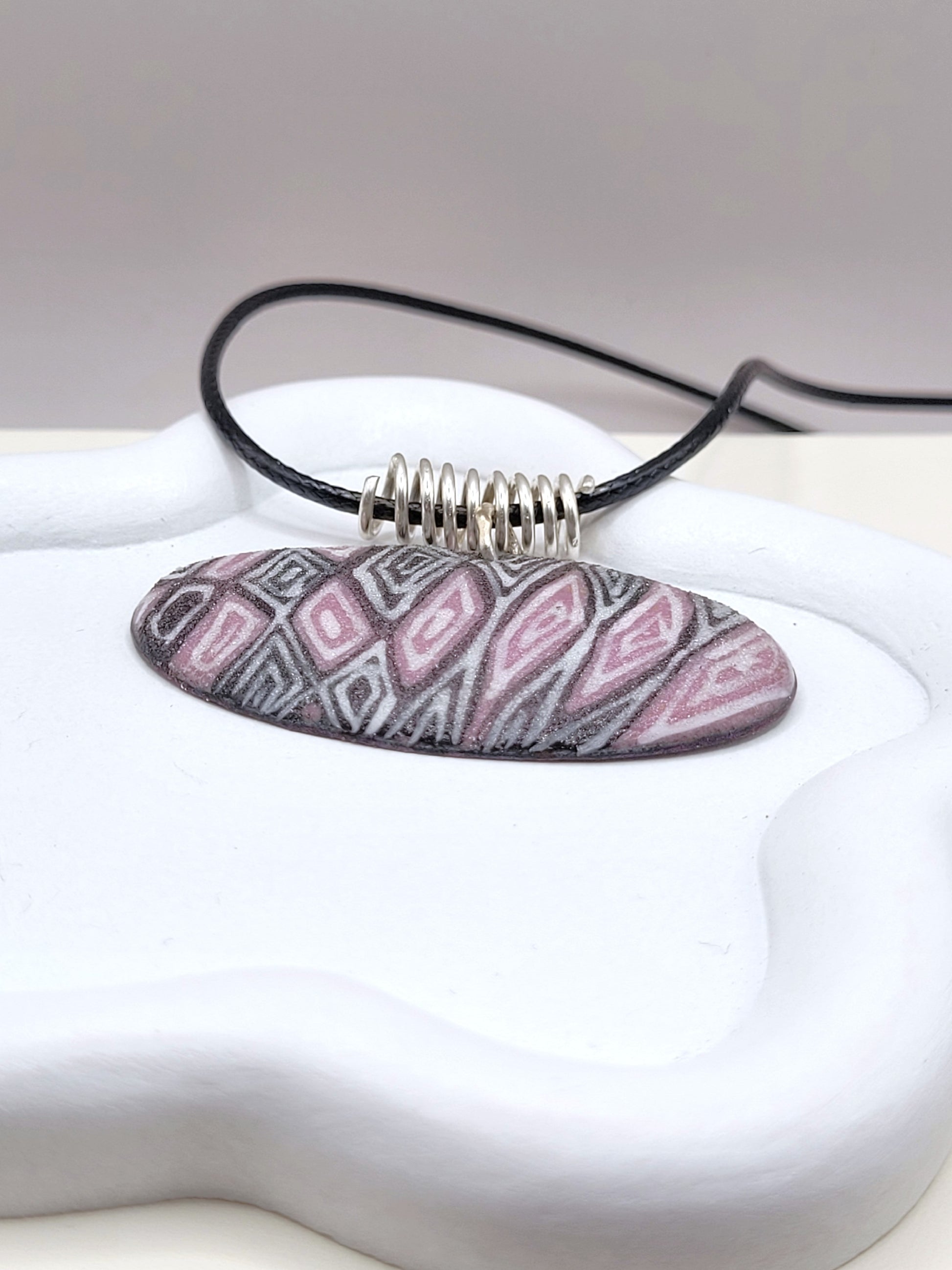 gros plan sur le pendentif ovale au design original inspiré par la lavande de provence chez maison calub émail sur cuivre opaque finition givrée mate émaux traditionnels fait à la main en provence belière en argent monté sur cordon