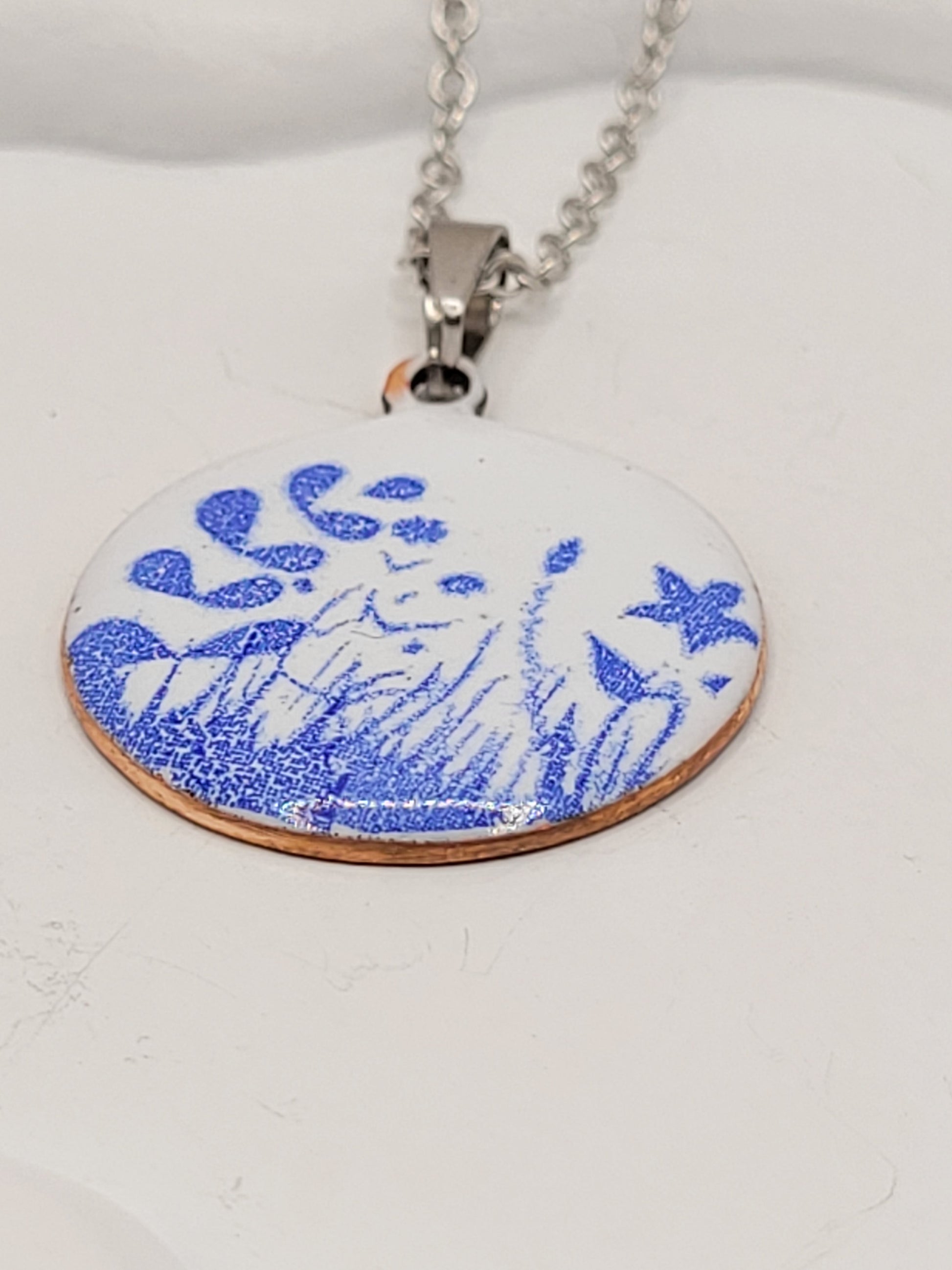 pendentif de la série porcelaine chez maison Calub. Pendentif rond en émail sur cuivre blanc porcelaine orné de fins motif floraux bleus, monté sur une fine chaine en acier.