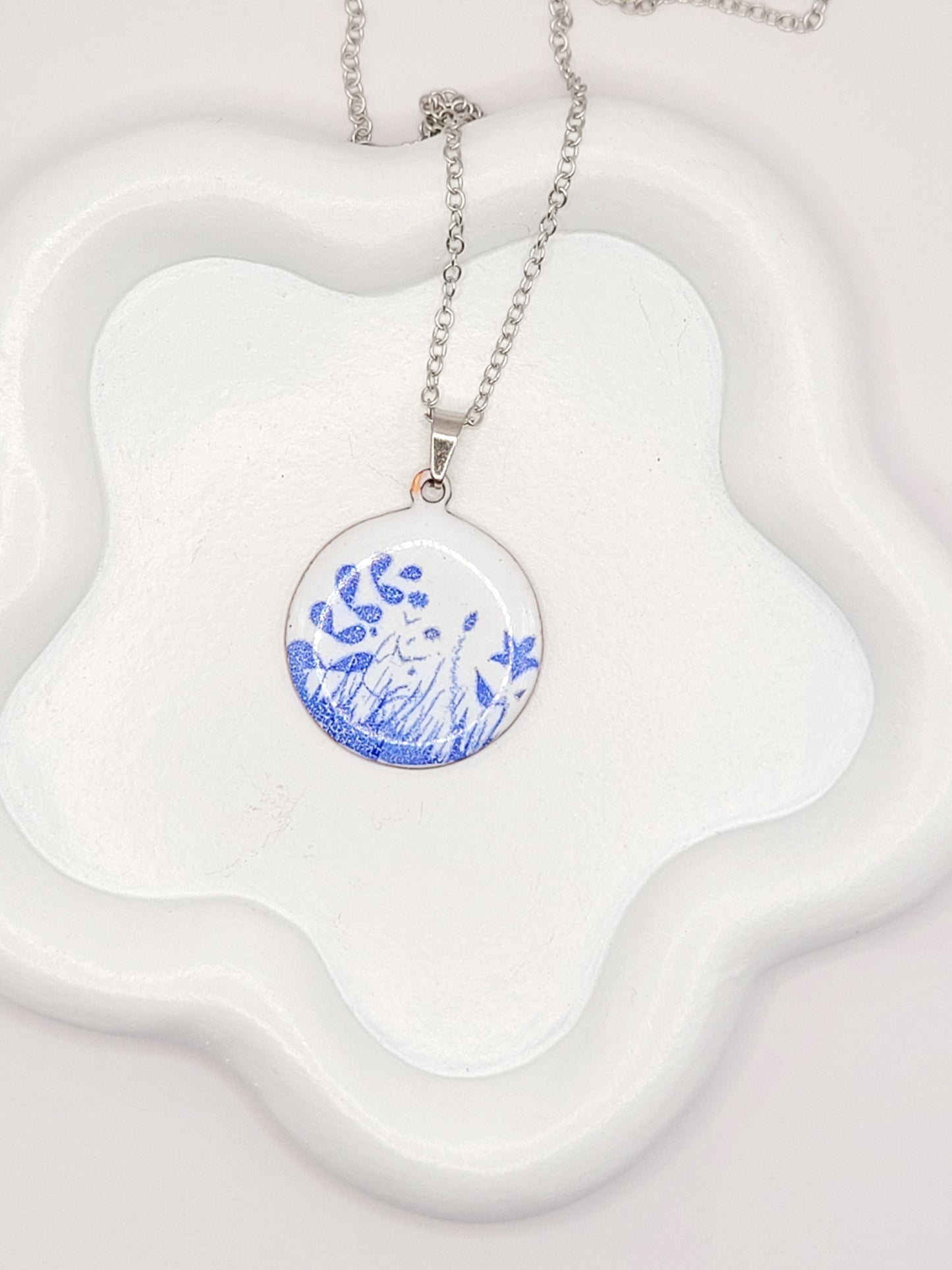 pendentif de la série porcelaine chez maison Calub. Pendentif rond en émail sur cuivre blanc porcelaine orné de fins motif floraux bleus, monté sur une fine chaine en acier.