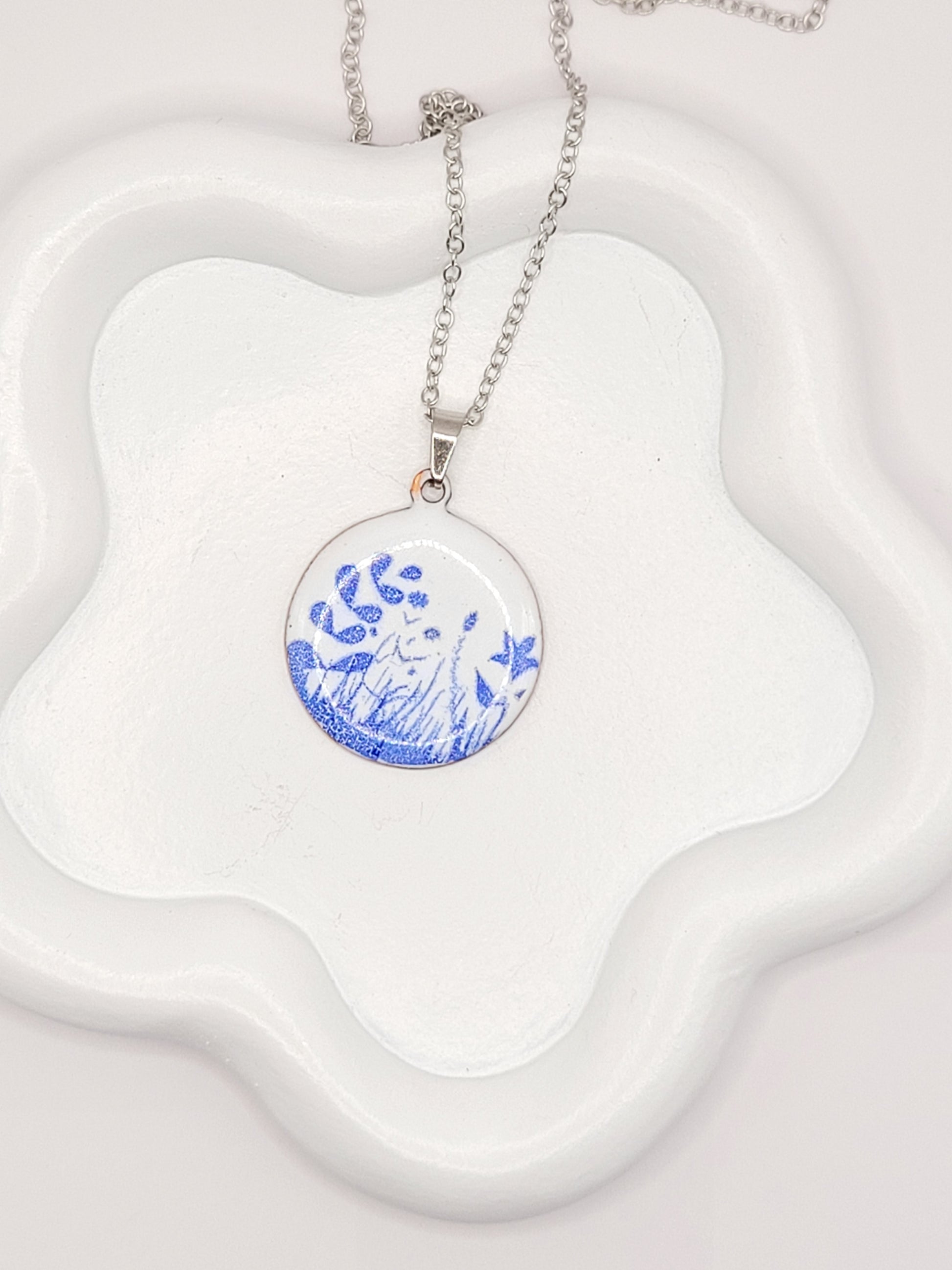 pendentif de la série porcelaine chez maison Calub. Pendentif rond en émail sur cuivre blanc porcelaine orné de fins motif floraux bleus, monté sur une fine chaine en acier.