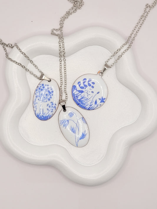 ensemble de 3 pendentifs de la série porcelaine chez maison Calub. Pendentif rond ou ovale en émail sur cuivre blanc porcelaine orné de fins motif floraux bleus, monté sur une fine chaine en acier.