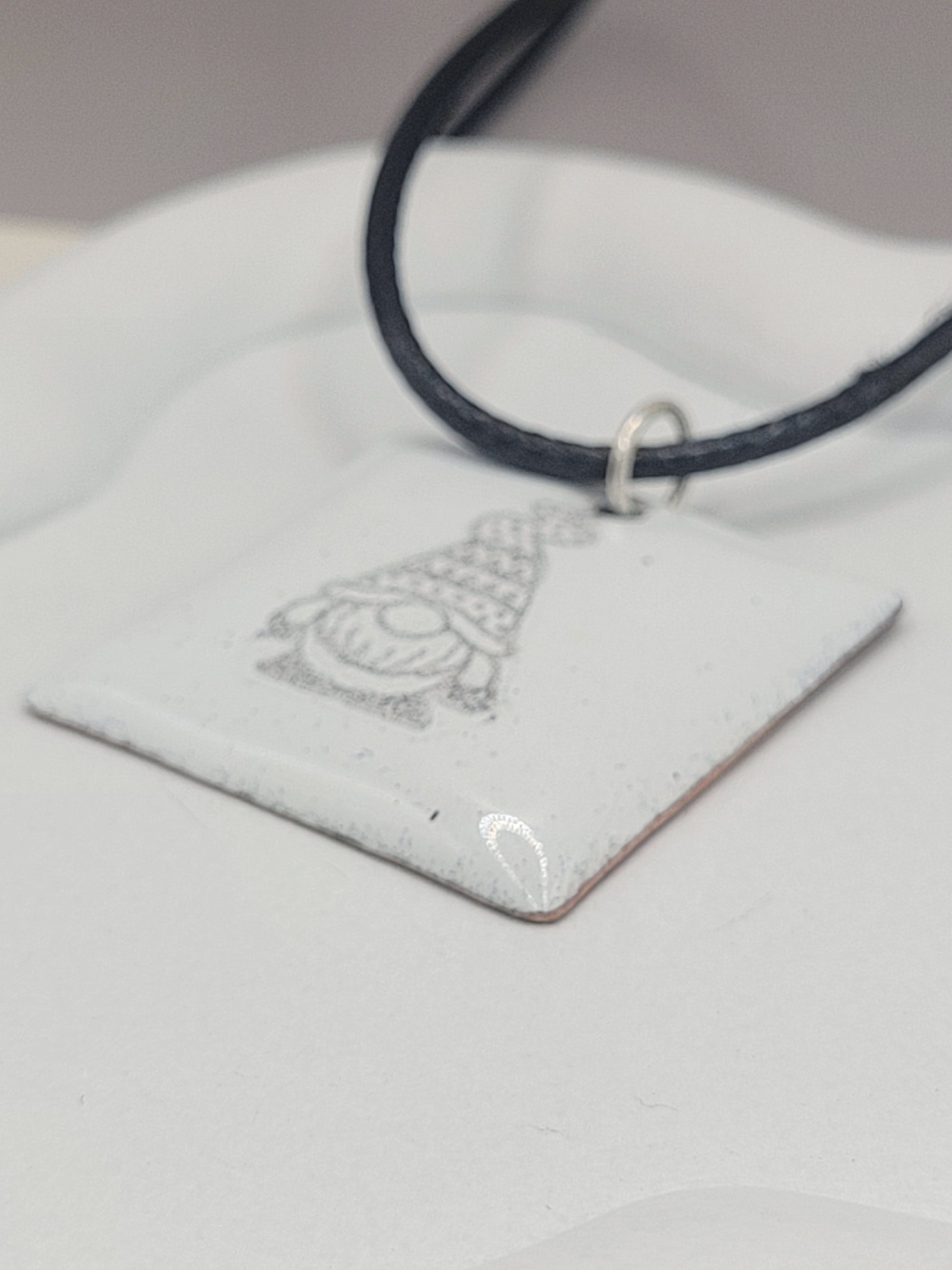 gros plan sur un petit pendentif carré blanc en émail au motif de petit lutin chez maison calub cadeau original